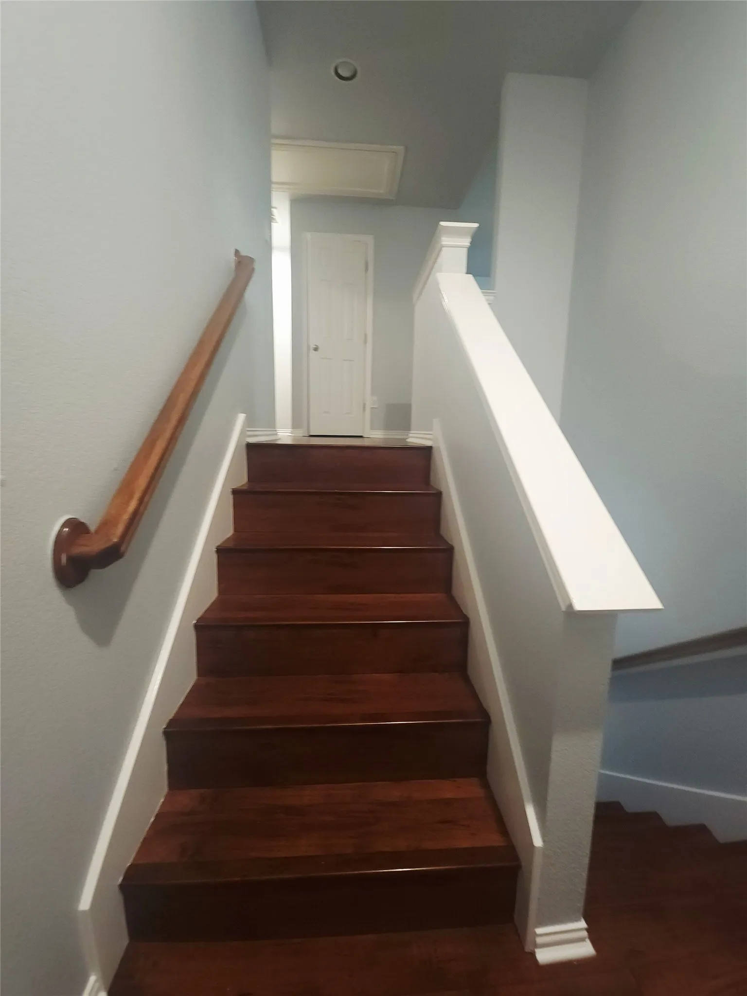 Hardwood stairwell with white trim and a coordinating wood handrail, set against neutral wall finishes