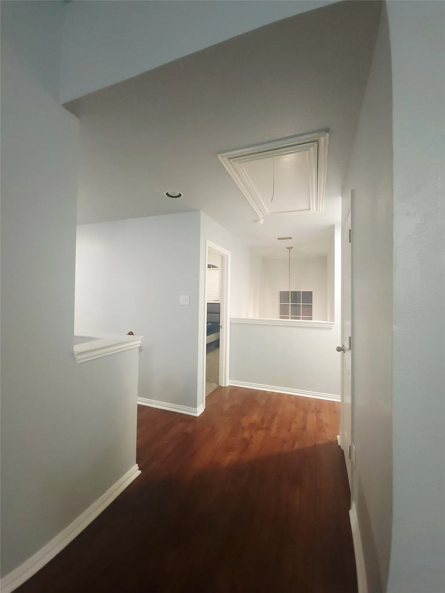 Hallway featuring wood-finish flooring, light grey painted walls, white baseboards, and white door trim