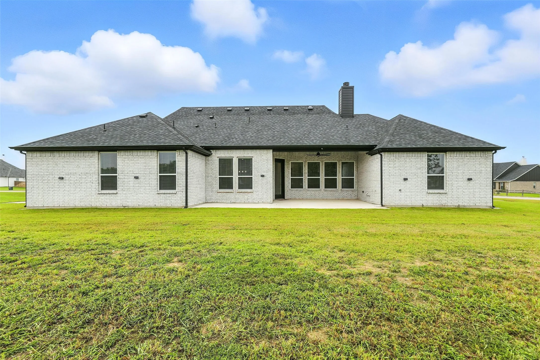 Spacious rear exterior featuring light-colored brick, dark shingle roofing, and a large concrete patio