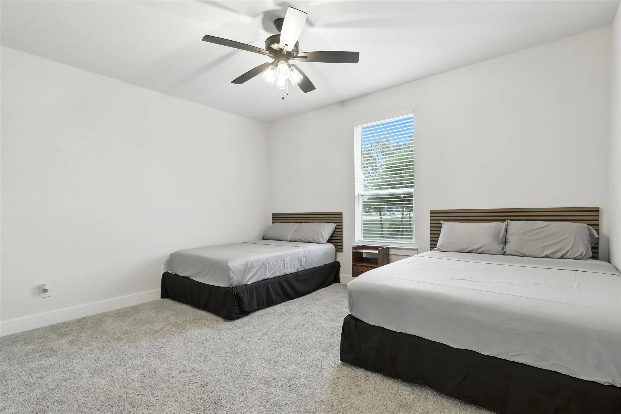 Bright room featuring a window with horizontal blinds, a ceiling fan with integrated lighting, and light-toned wall-to-wall carpeting
