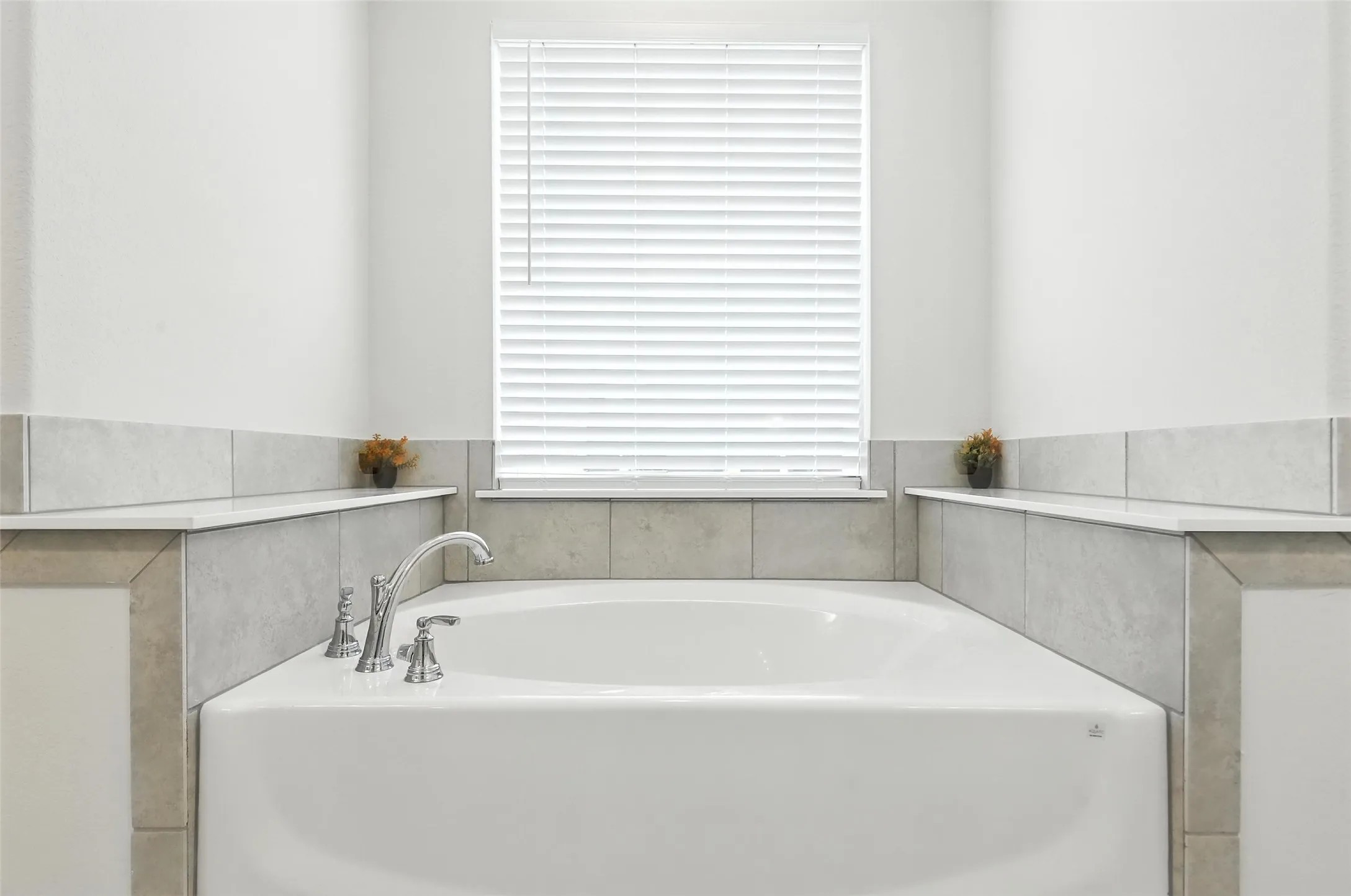Built-in soaking tub featuring chrome fixtures, a tiled surround, integrated shelving, and a window with privacy blinds