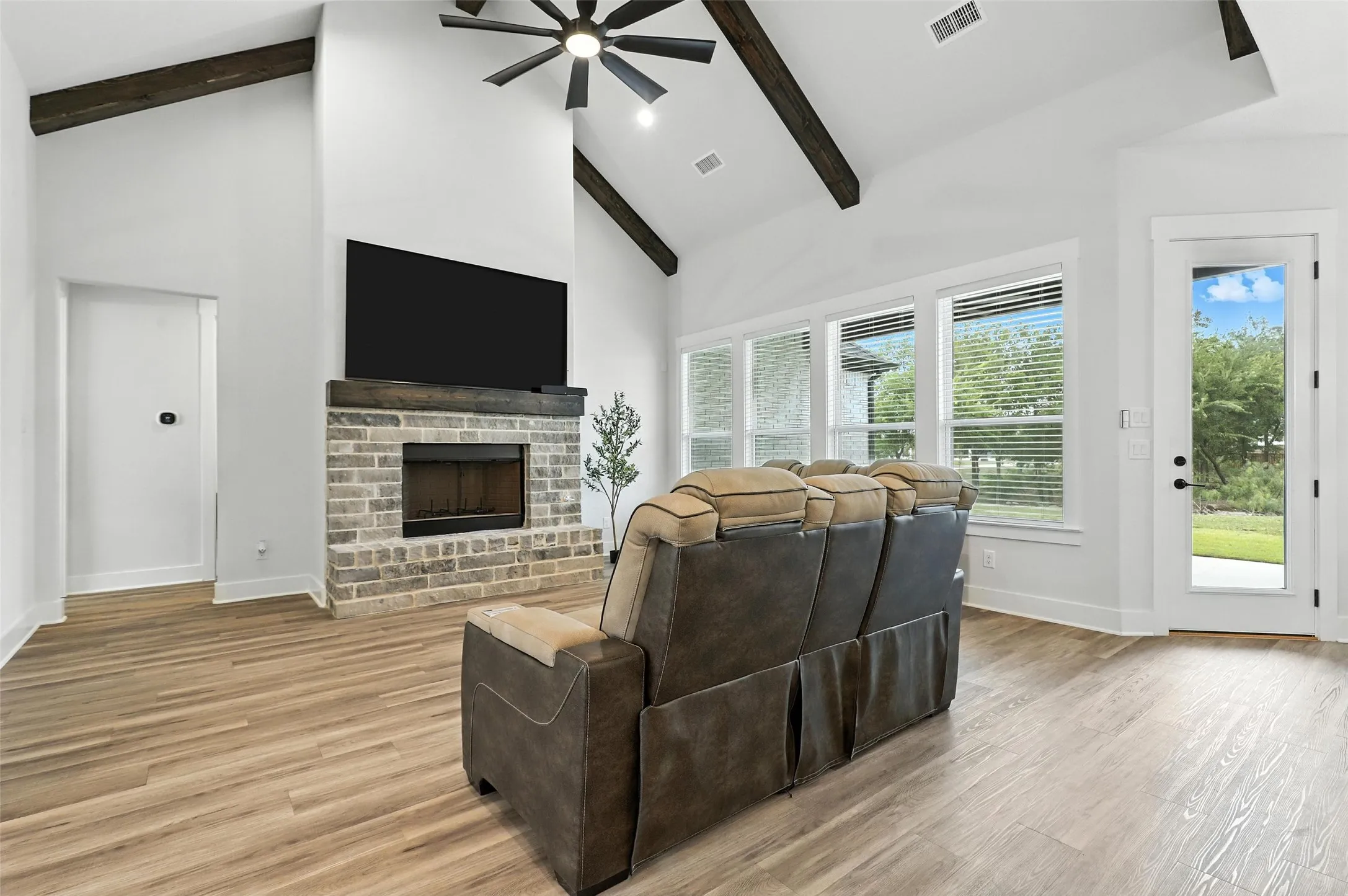 Contemporary brick exterior with dark trim accents, a prominent front gable, a multi-pane wood-finish entry door, and a spacious green lawn