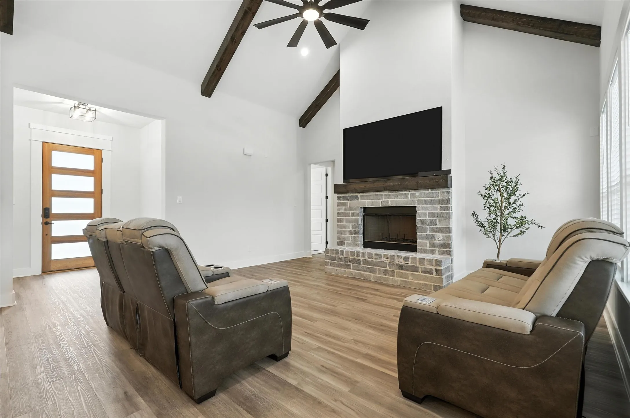 Spacious living area featuring a vaulted ceiling with exposed wood beams, a ceiling fan, and wood-finish flooring