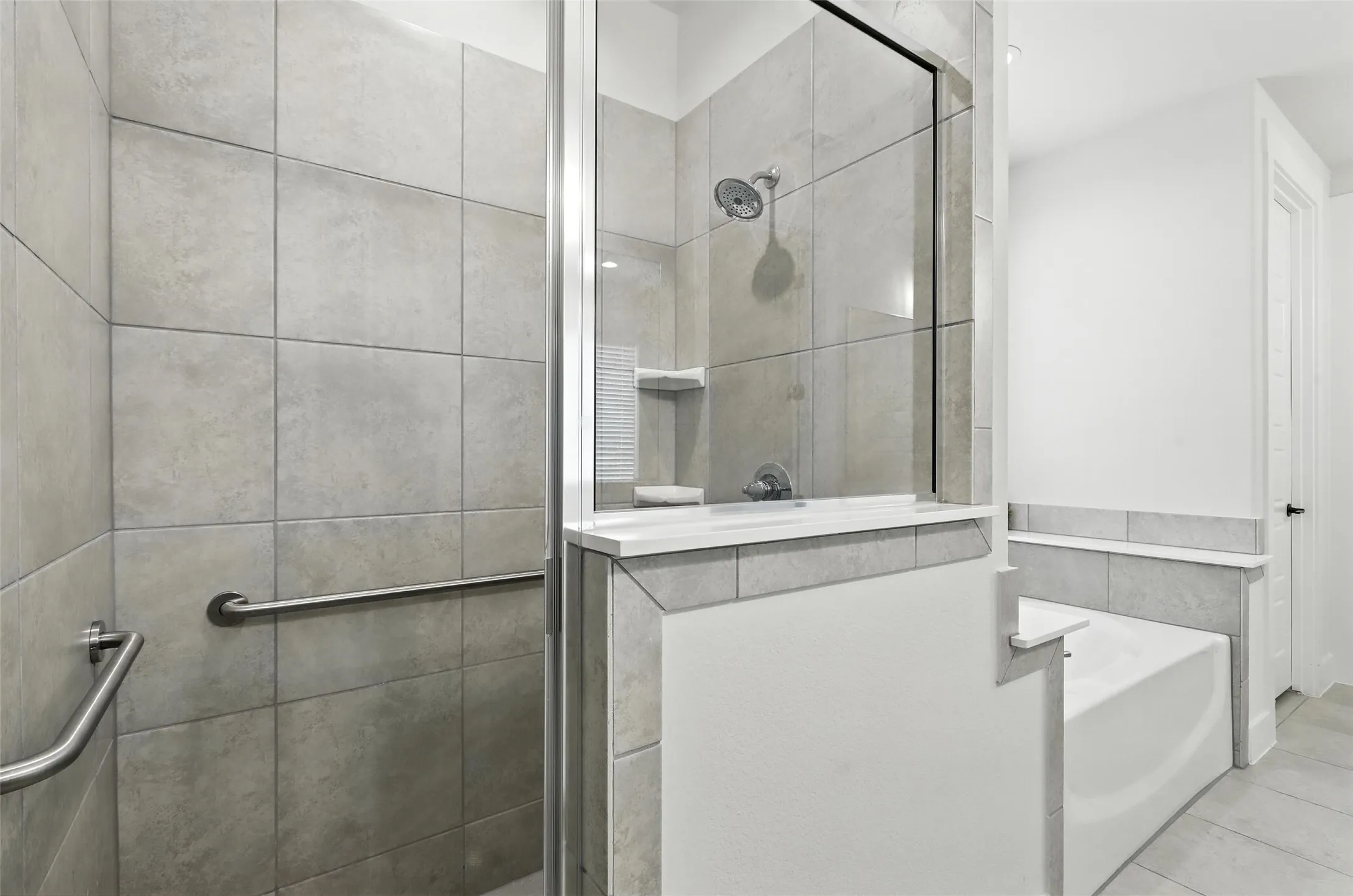 Contemporary bathroom featuring a tiled shower with glass enclosure, a built-in shower shelf, a showerhead, a separate soaking tub, and grab bars