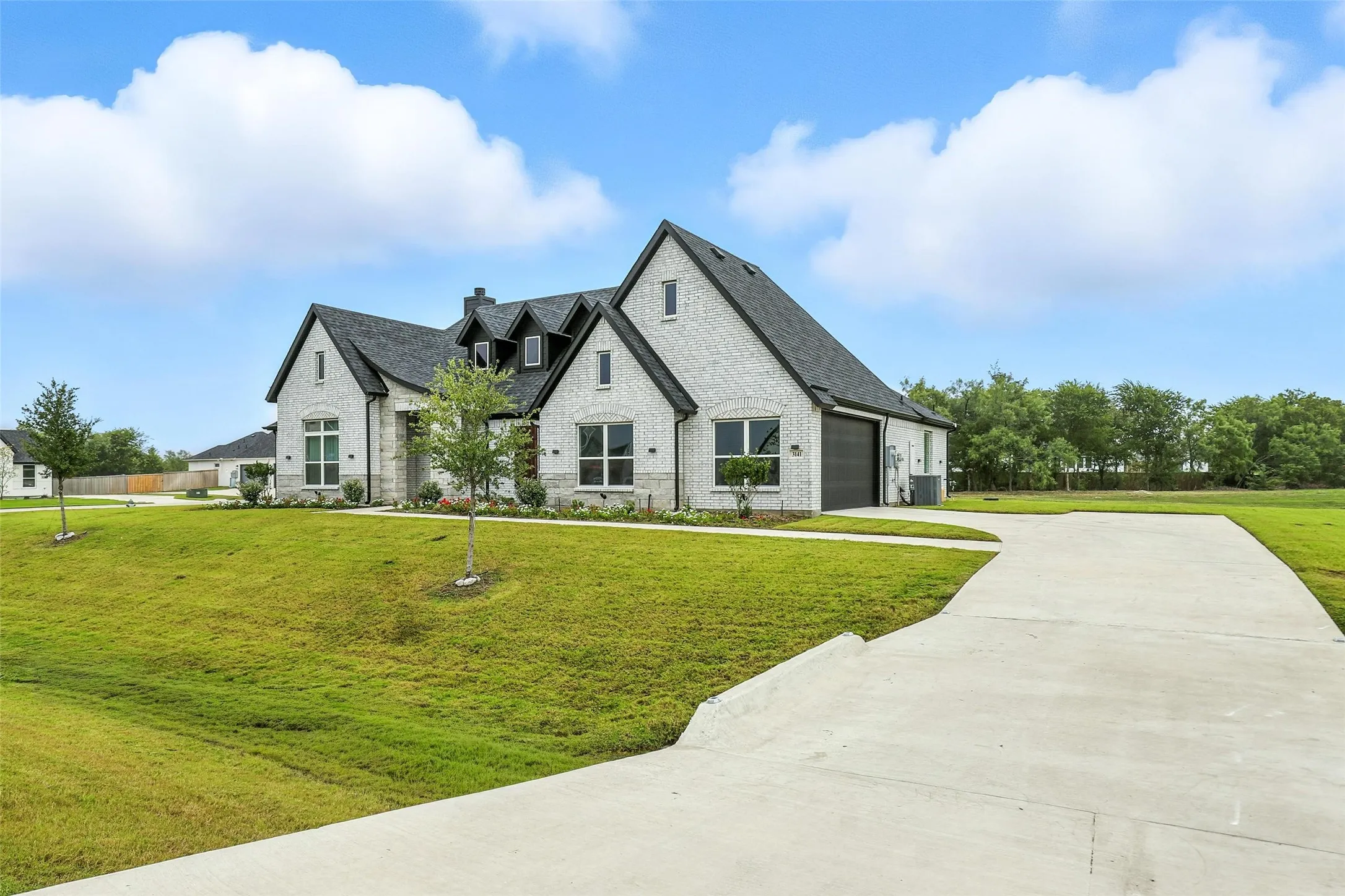 Modern farmhouse architecture featuring light-colored brick, a dark shingle roof, and multiple gables
