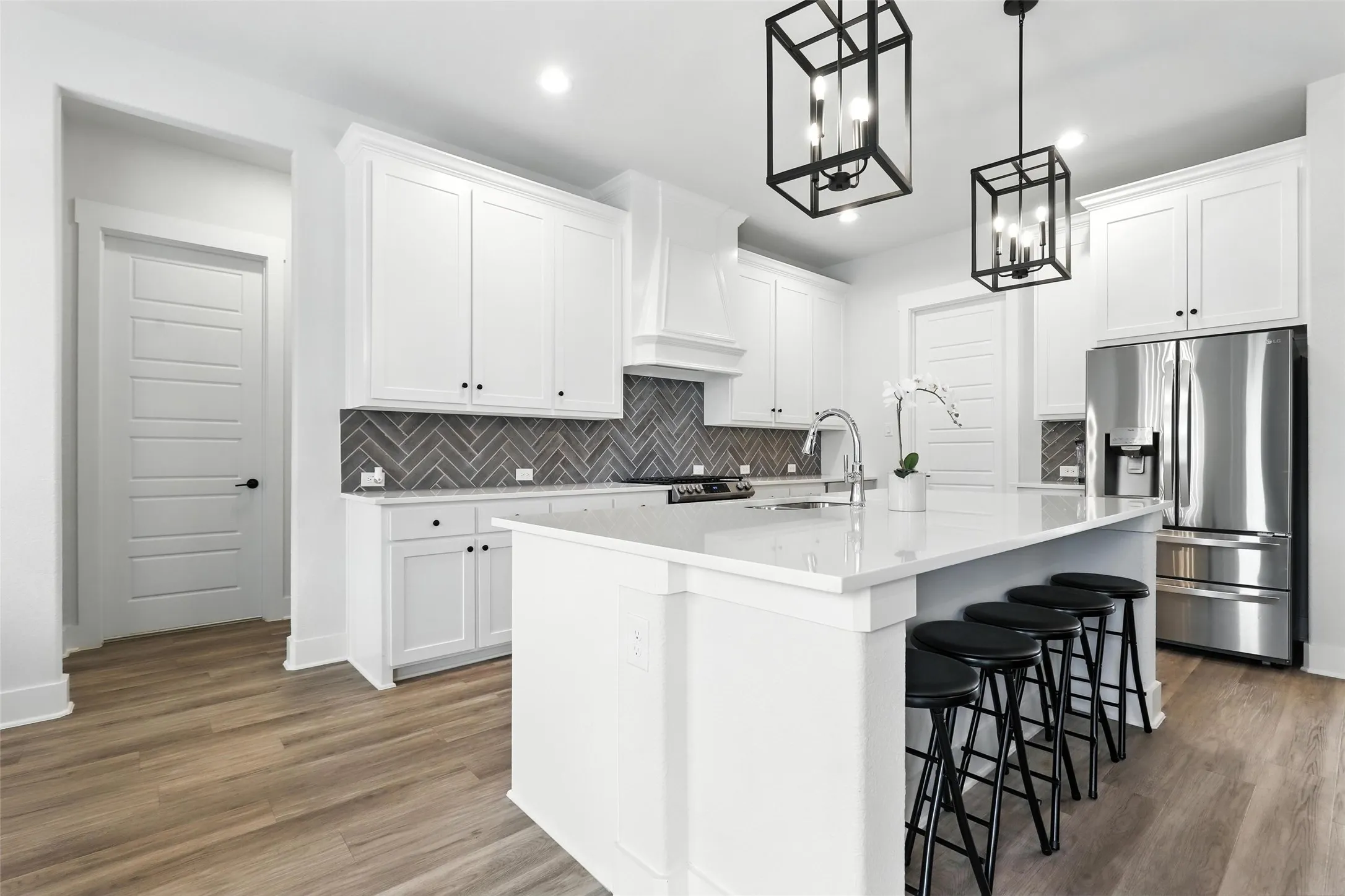 Modern kitchen featuring a large central island with seating, white shaker cabinetry, stainless steel appliances, and wood-finish flooring