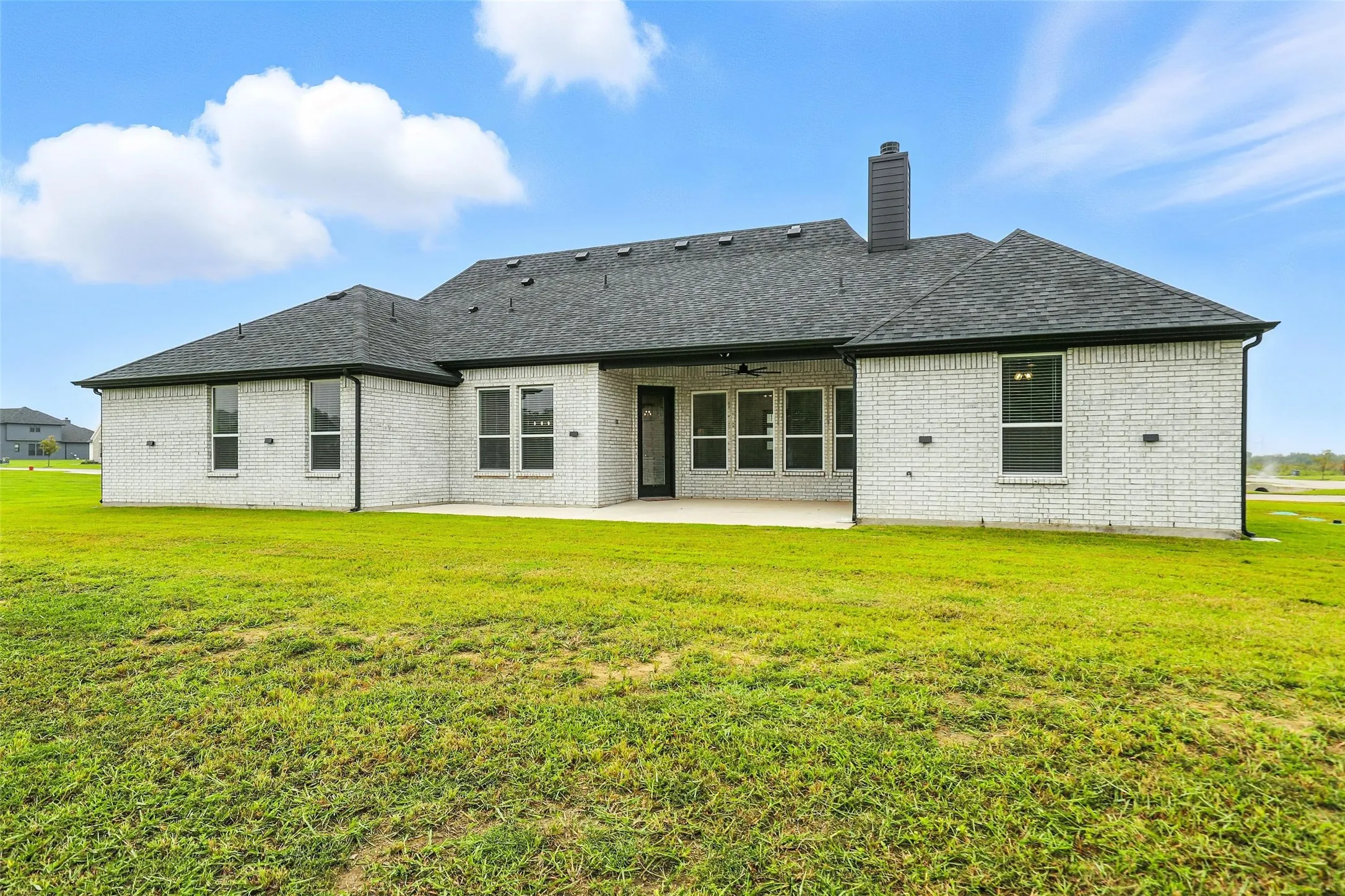 White brick exterior with a dark shingle roof and a concrete patio