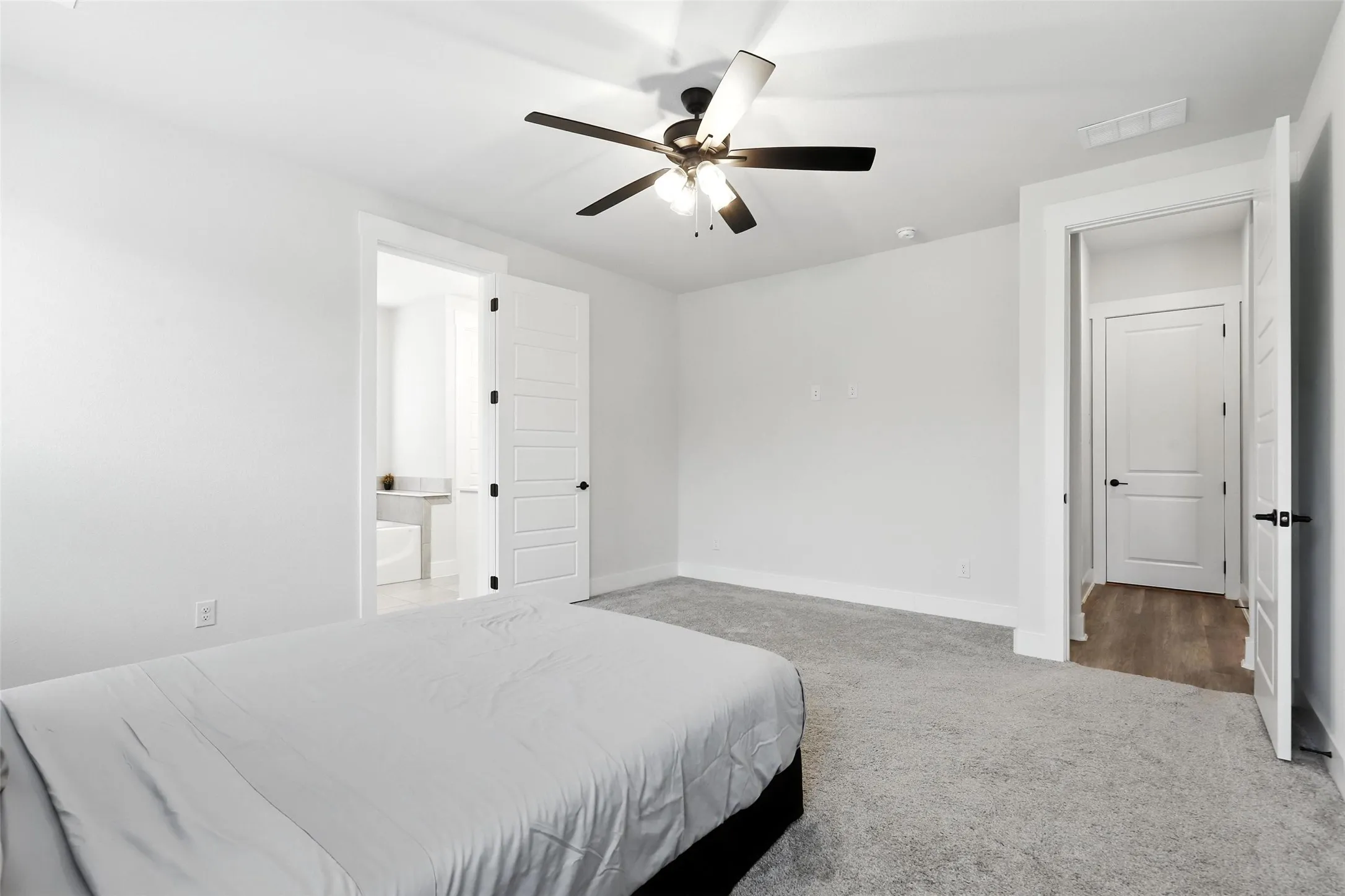 Carpeted bedroom featuring white walls, a ceiling fan with integrated lighting, and white paneled doors with matte black hardware
