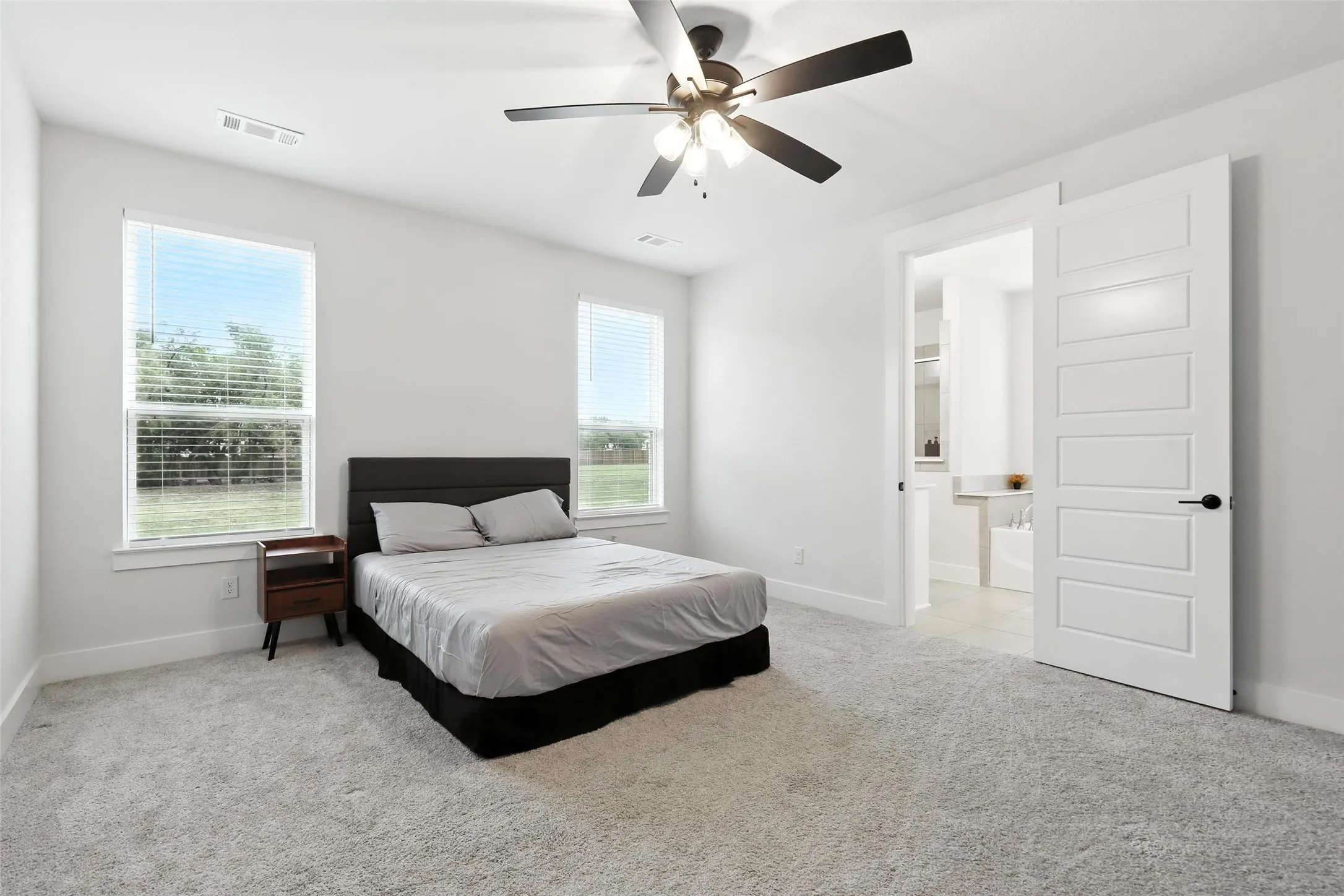 Carpeted room featuring a ceiling fan with integrated lighting, two windows with blinds, and a five-panel interior door