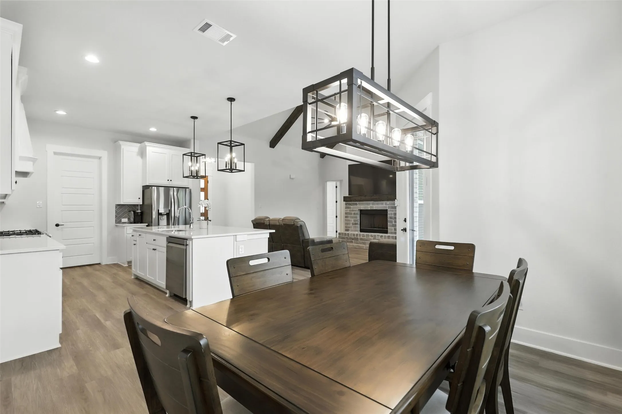 Open-concept living space featuring wood-finish flooring, a kitchen with white cabinetry and an island, a stainless steel dishwasher, and a living area with a stone-surround fireplace