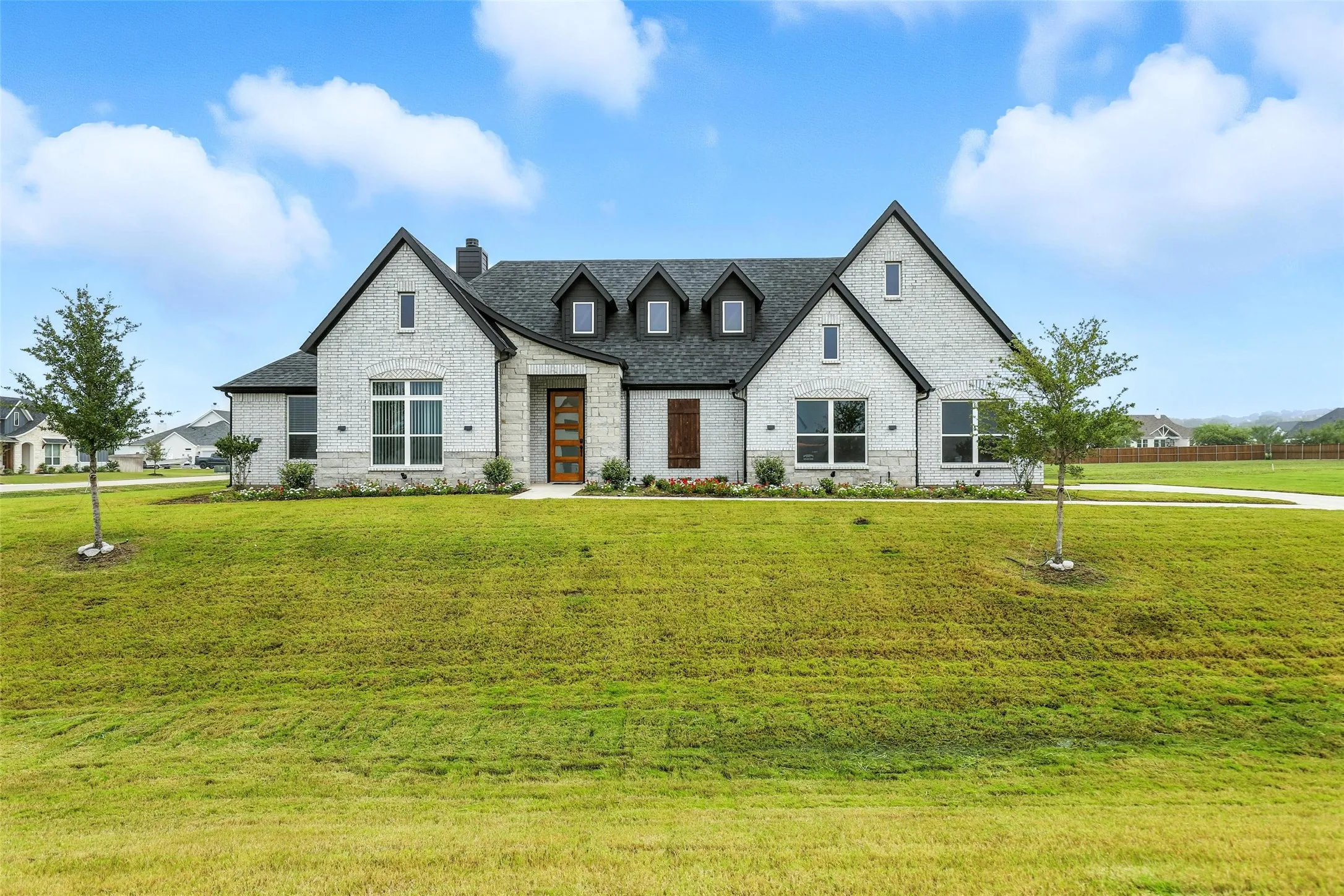 Contemporary brick exterior with dark trim accents, a prominent front gable, a multi-pane wood-finish entry door, and a spacious green lawn