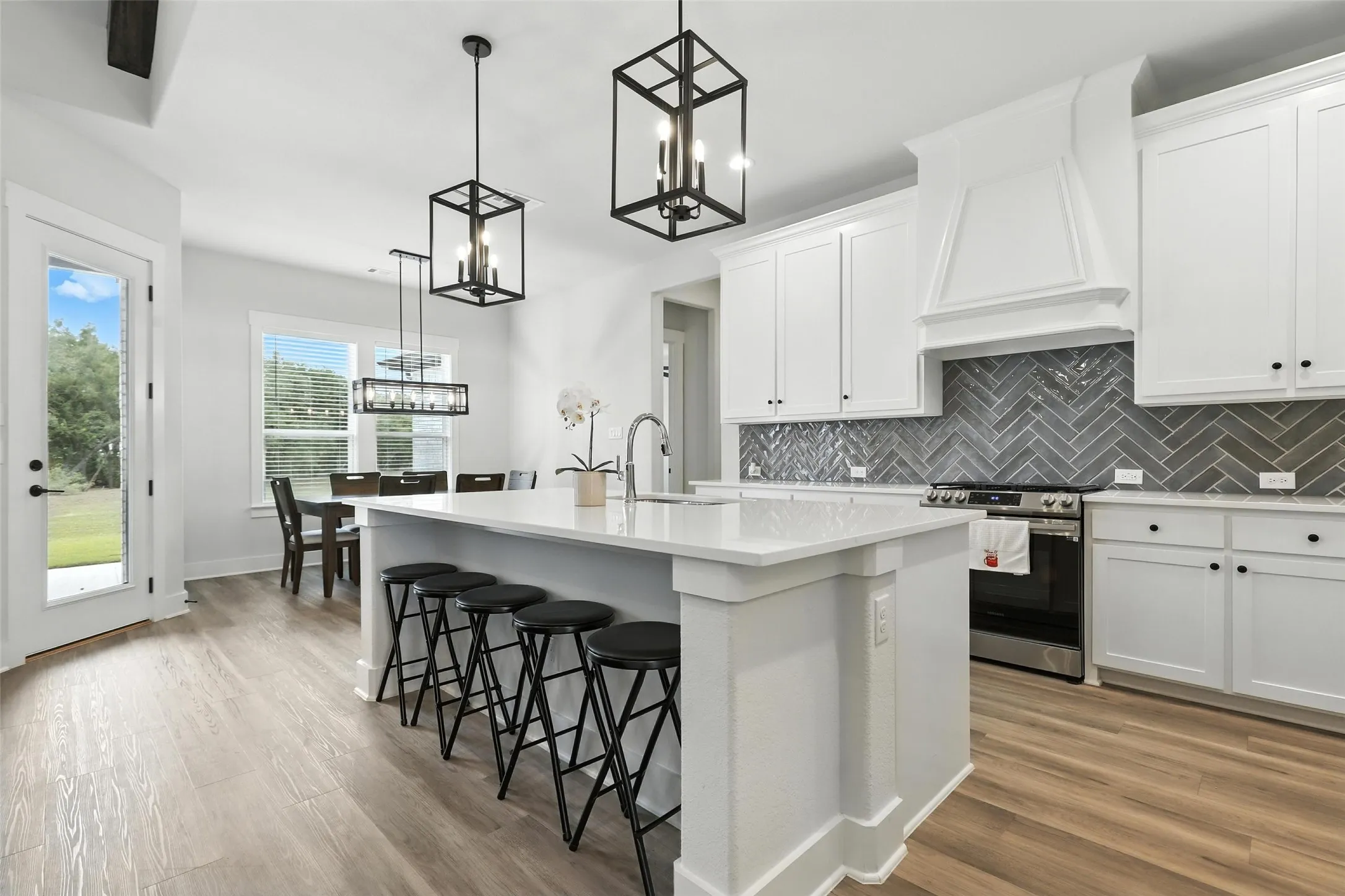 Modern kitchen featuring a large island with seating, white cabinetry, herringbone tile backsplash, and wood-finish flooring