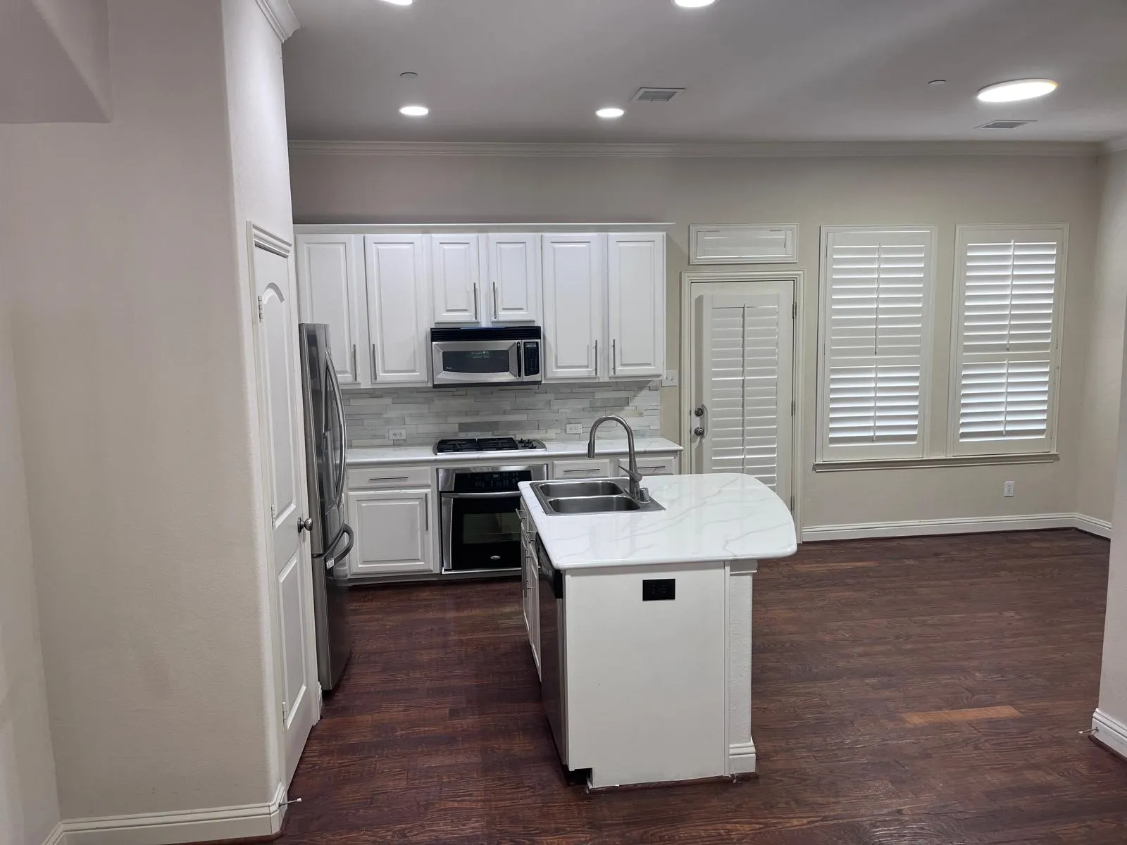 Modern kitchen featuring white cabinetry, a light-toned tile backsplash, stainless steel appliances, and a central island with an undermount sink