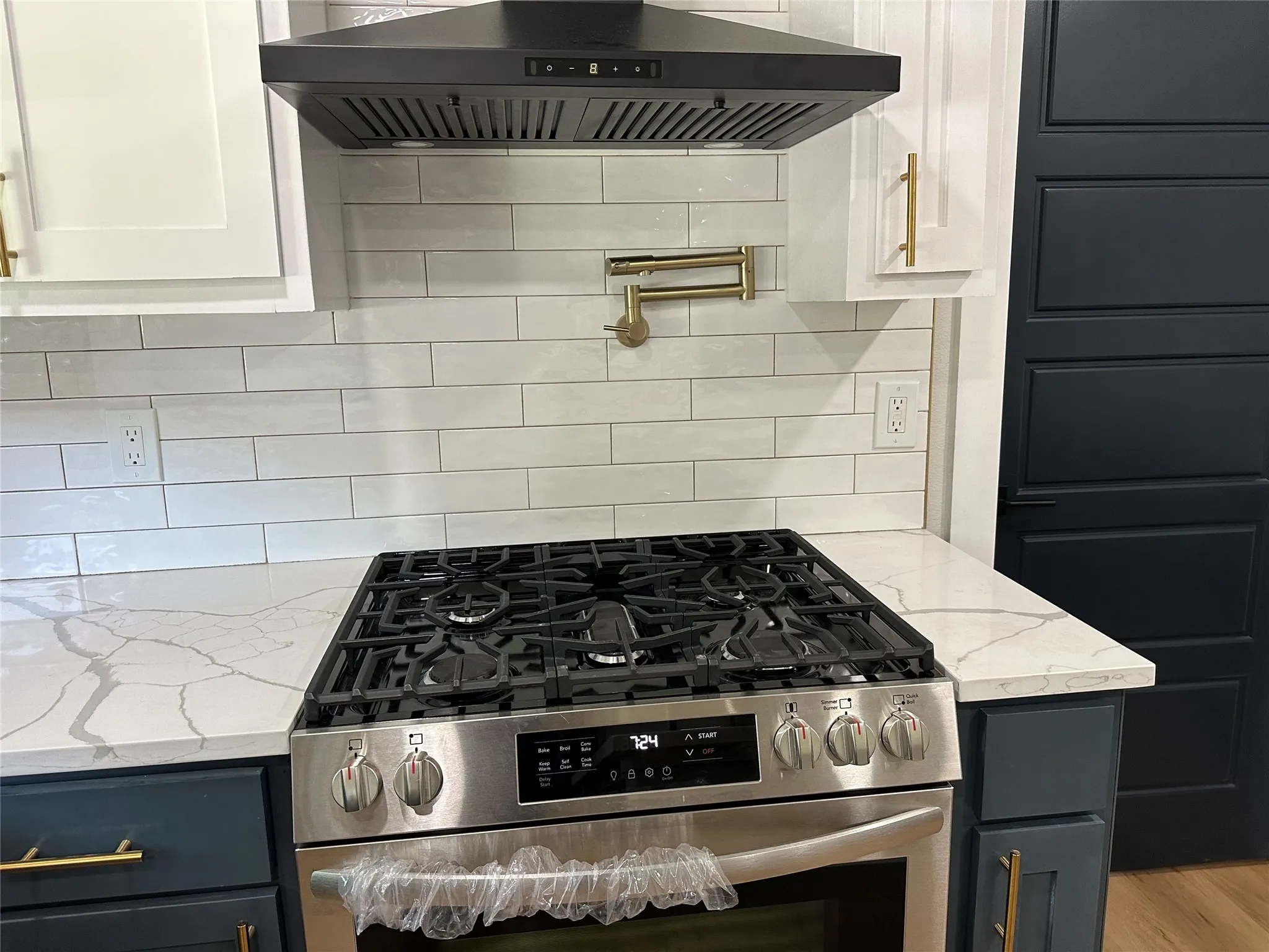 Kitchen with wall chimney range hood, white cabinets, stainless steel gas range, and tasteful backsplash