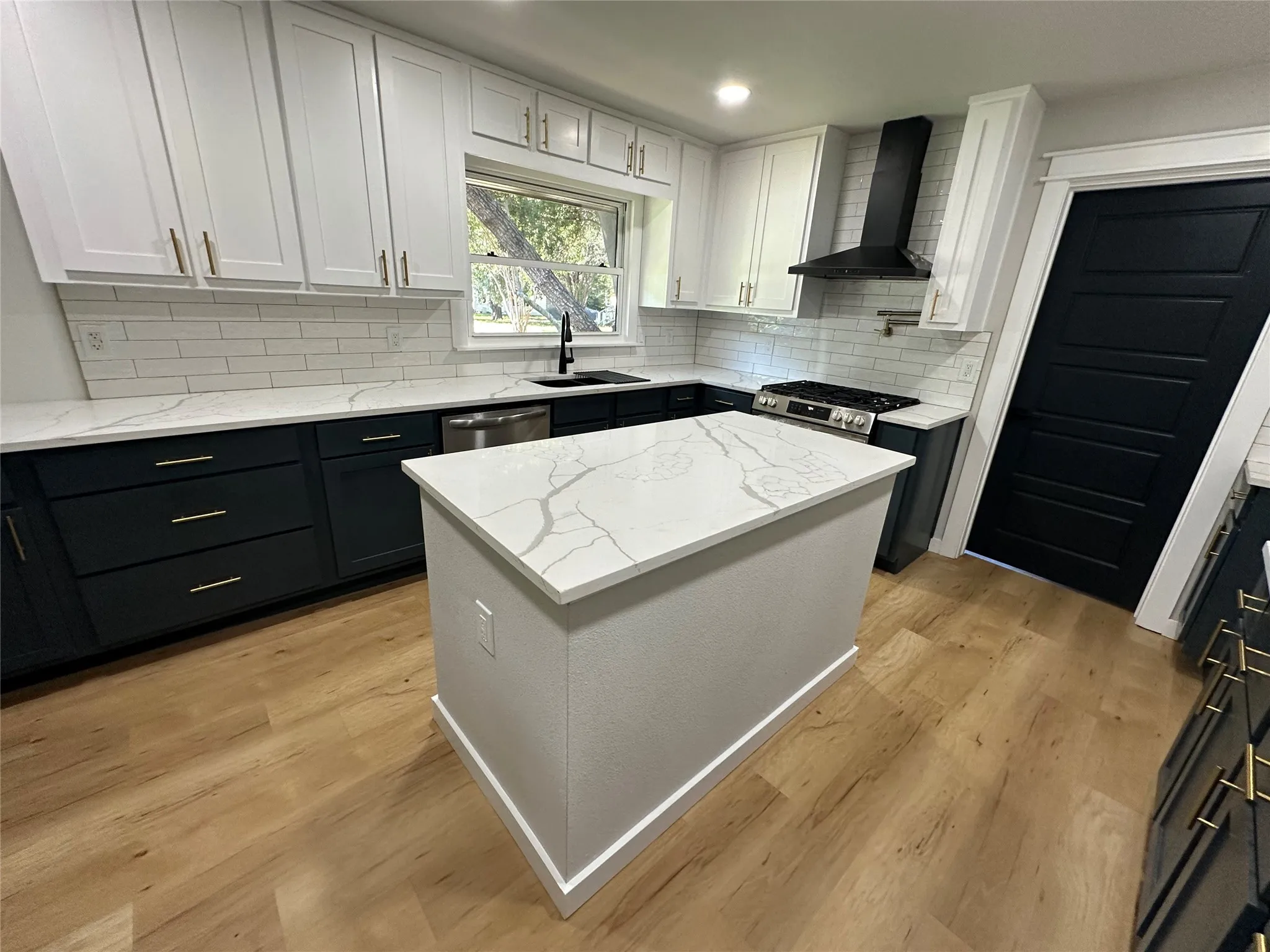 Kitchen featuring light hardwood / wood-style flooring, tasteful backsplash, wall chimney exhaust hood, white cabinets, and sink
