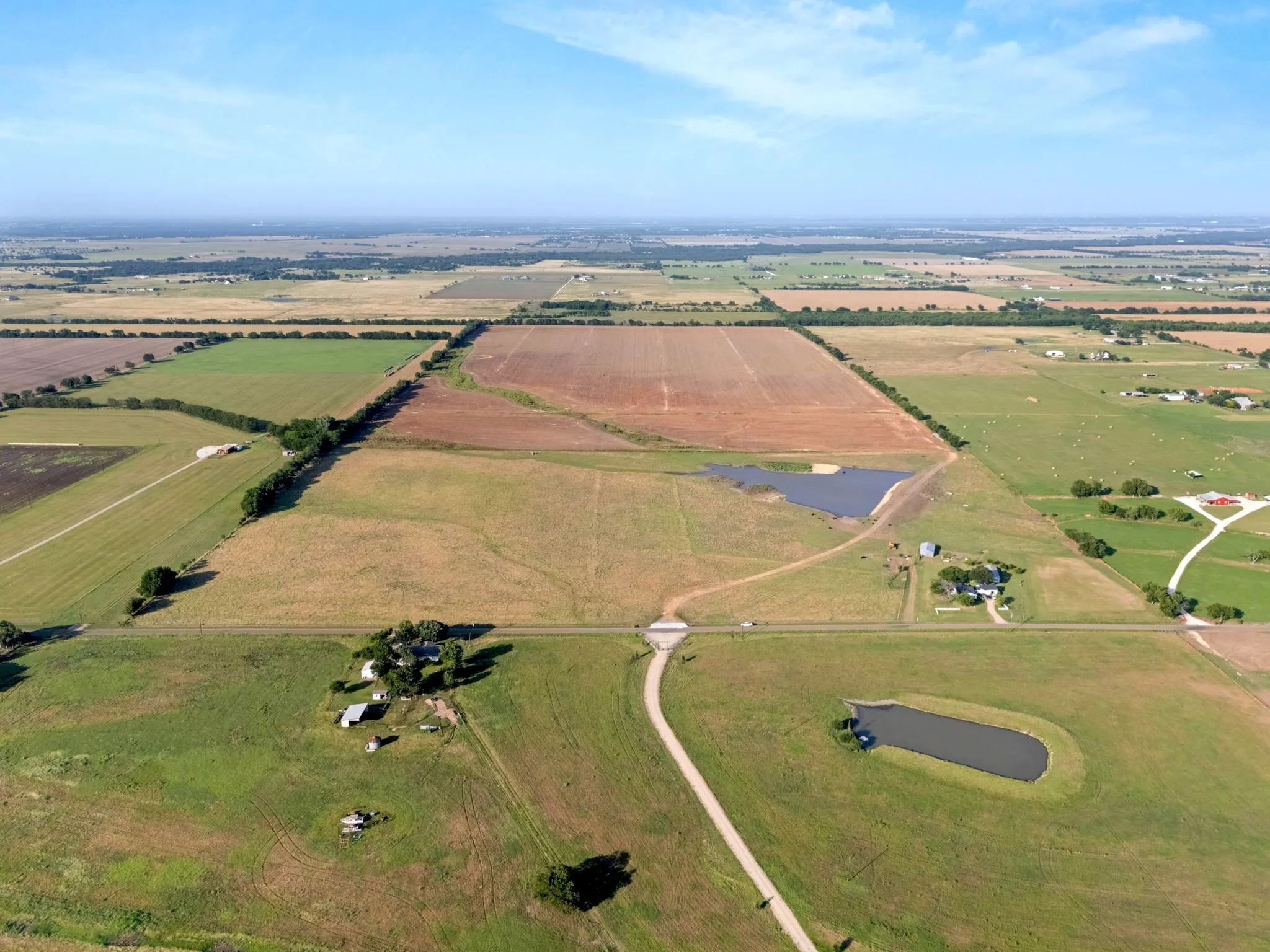 Expansive aerial view showcasing multiple parcels of agricultural land, two distinct ponds, and a winding unpaved road