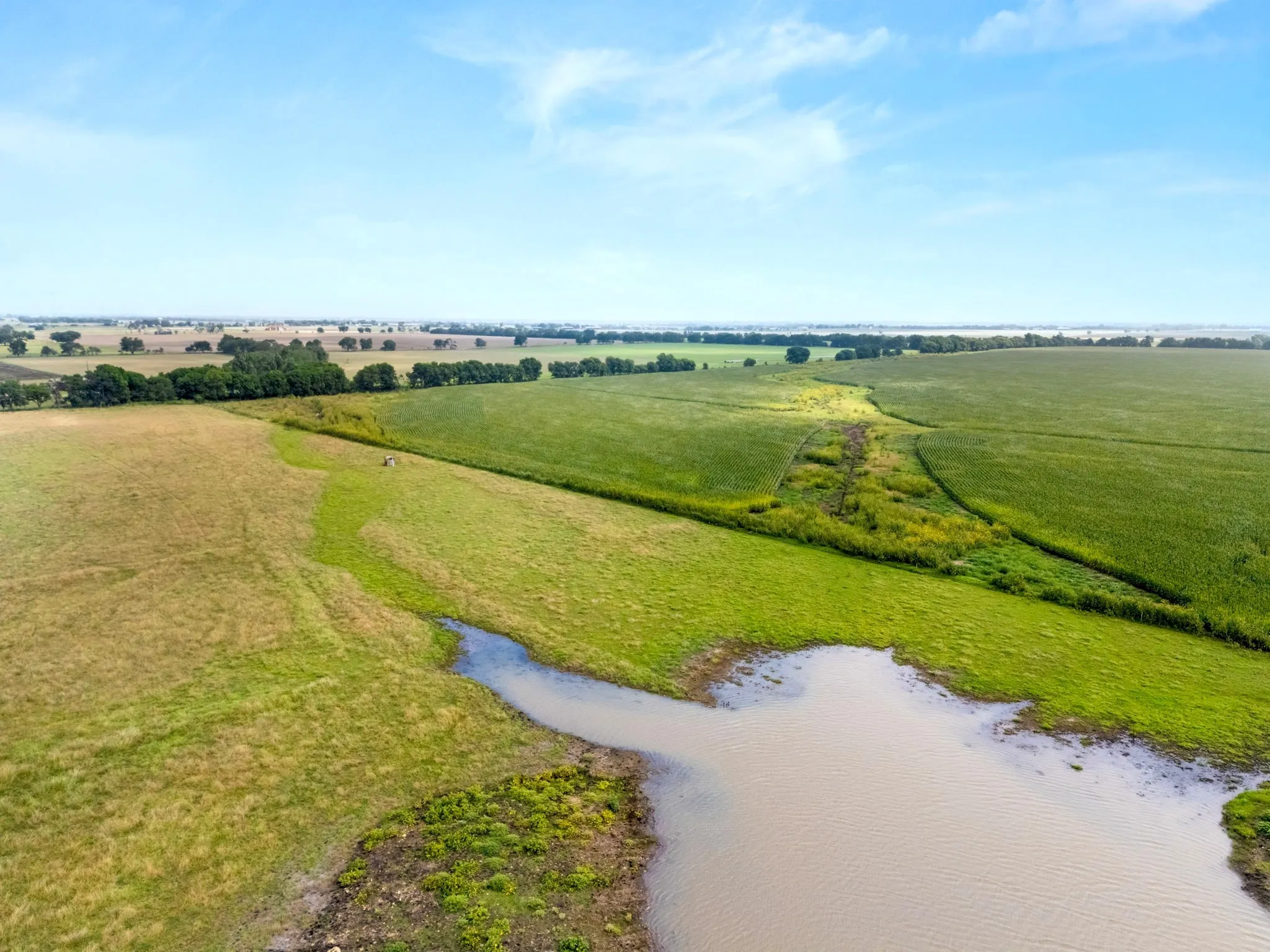 Expansive land parcel featuring a natural water body, varied terrain with both cultivated fields and open pasture, and a distant tree line
