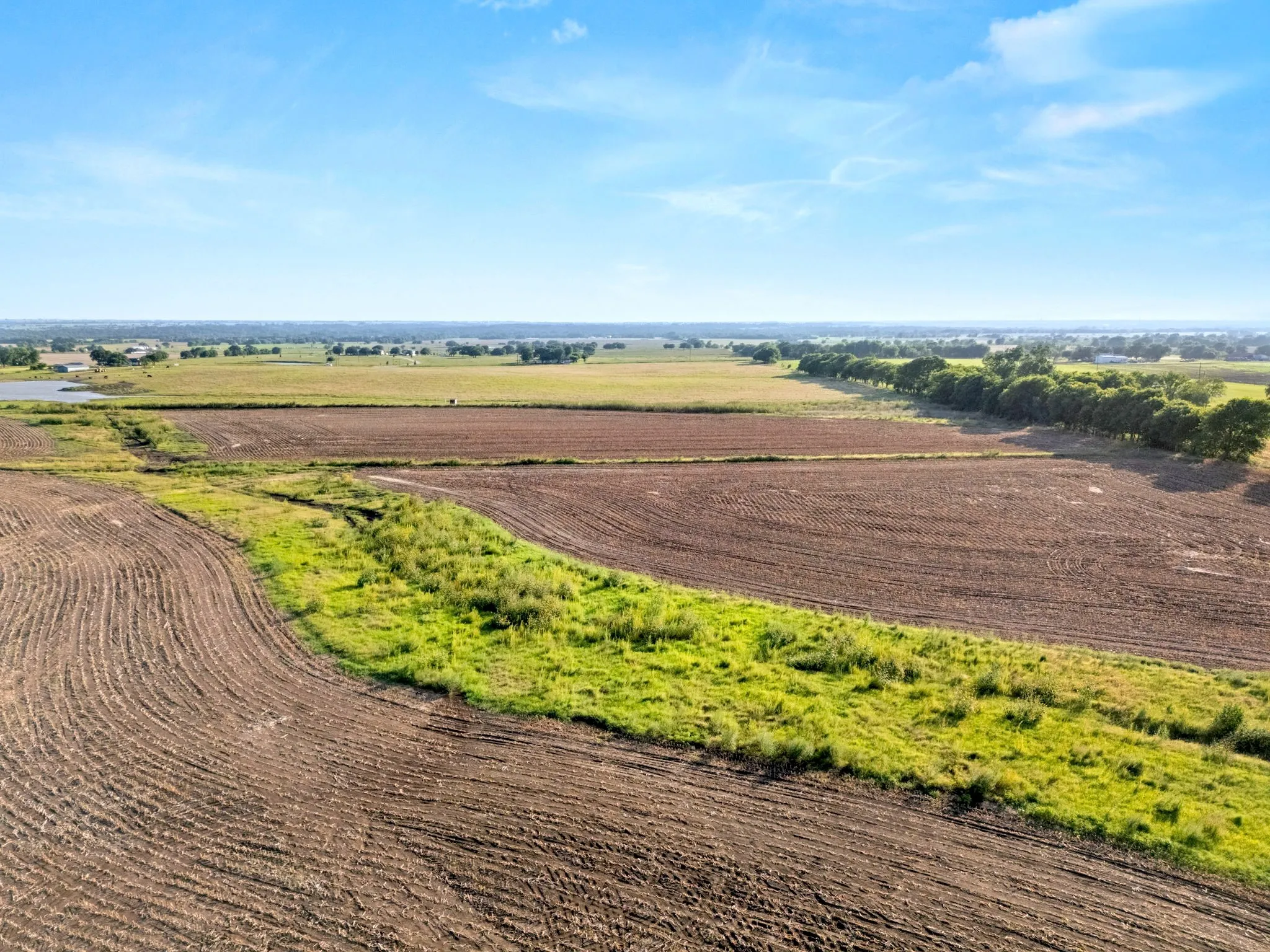 Expansive cultivated land featuring tilled fields, green pasture, and a distant body of water
