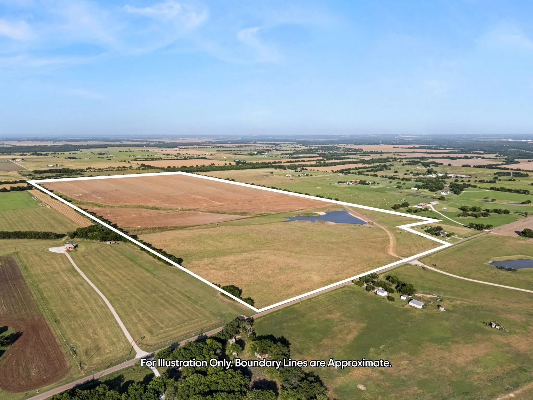 Expansive agricultural land featuring a large open field, an apparent pond, and surrounding green spaces