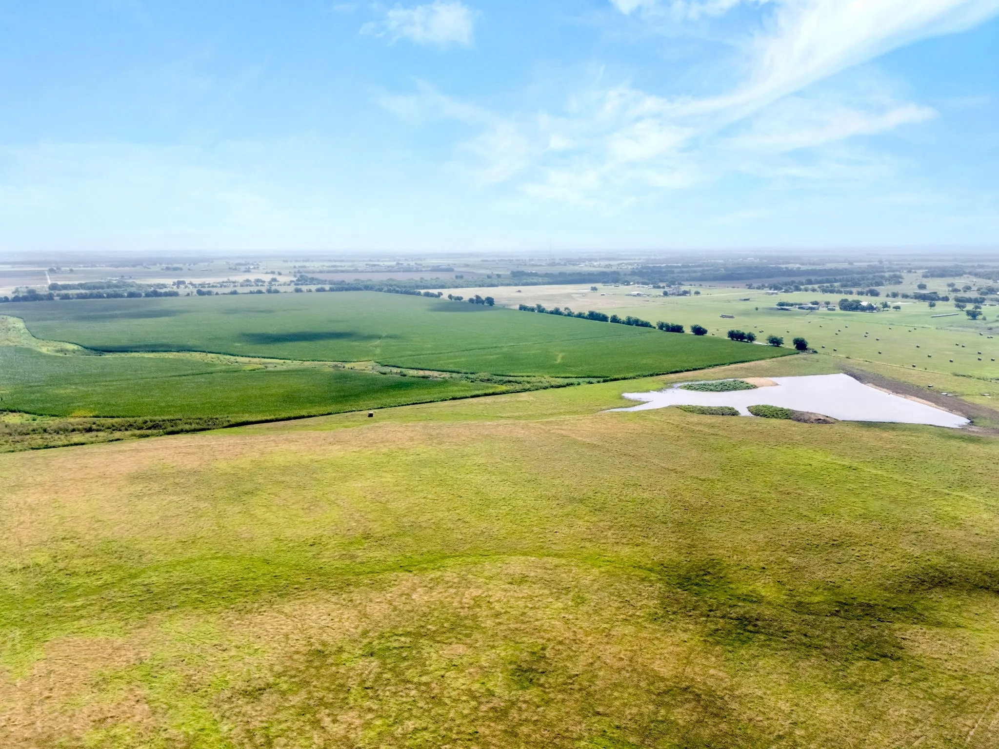 Expansive open land featuring a large pond, verdant agricultural fields, and scattered mature trees