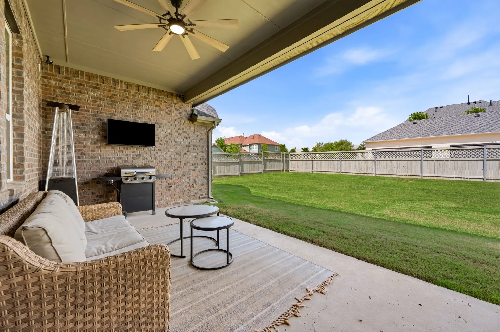 Covered patio featuring a brick exterior wall, a ceiling fan with integrated lighting, and a mounted flat-screen television