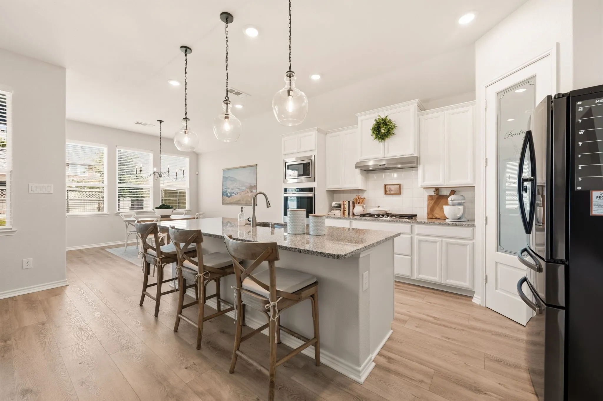 Contemporary kitchen featuring a large island with granite countertops, light wood-finish flooring, white cabinetry, a subway tile backsplash, and stainless steel appliances