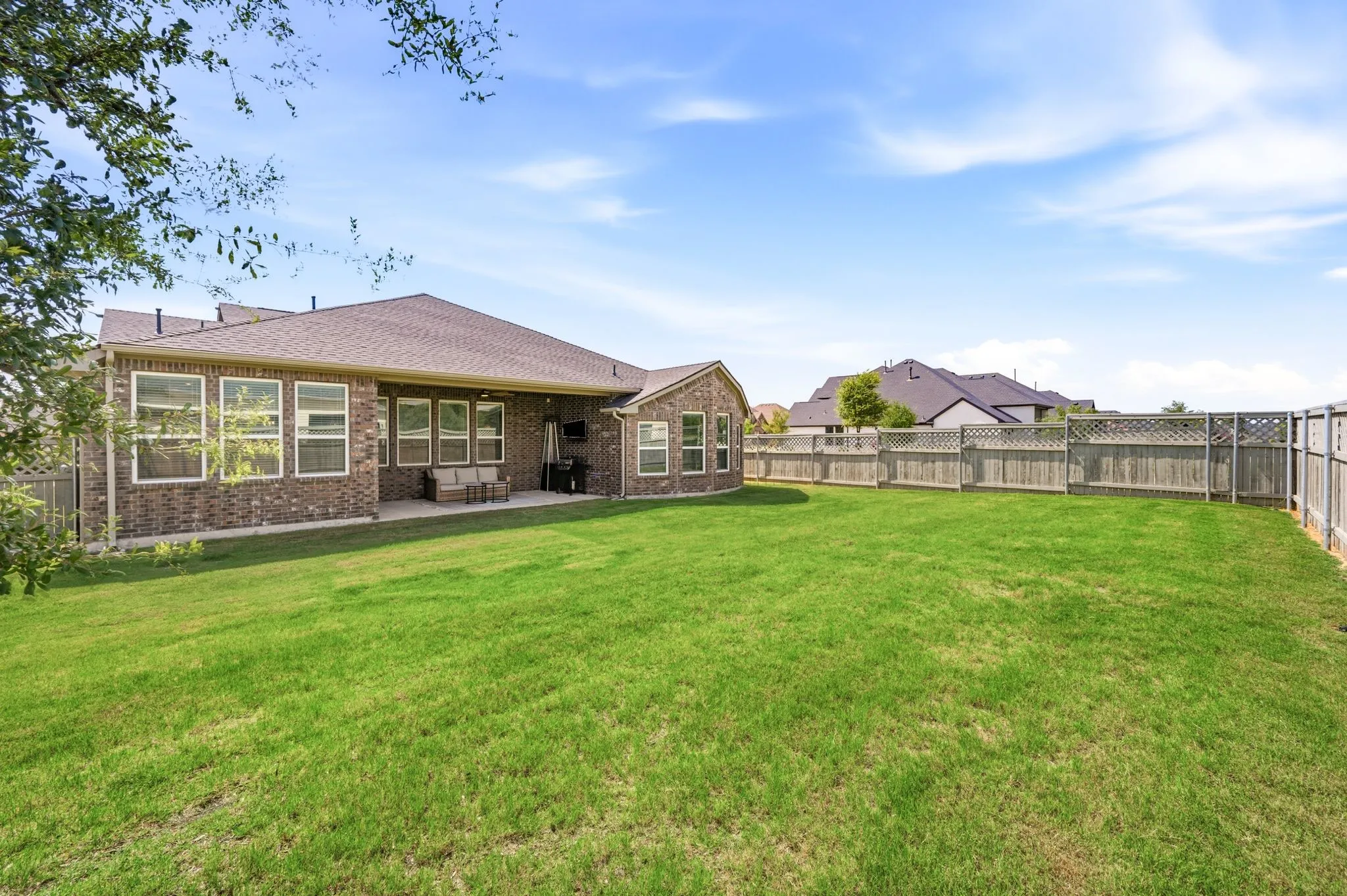 Expansive grassy yard featuring a brick exterior, multiple windows, a covered patio, and a wooden privacy fence