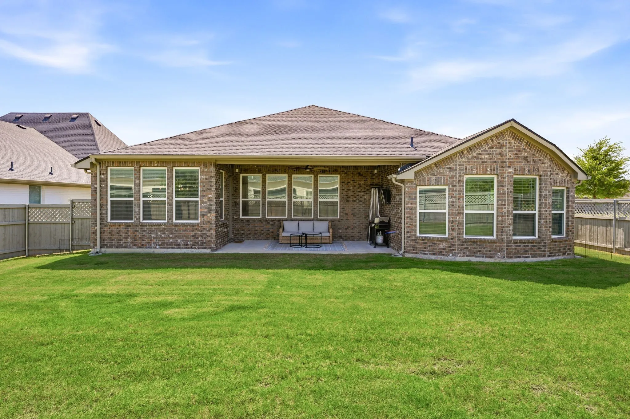 Expansive green lawn with a full brick exterior featuring a covered patio, multiple windows, and a fenced perimeter