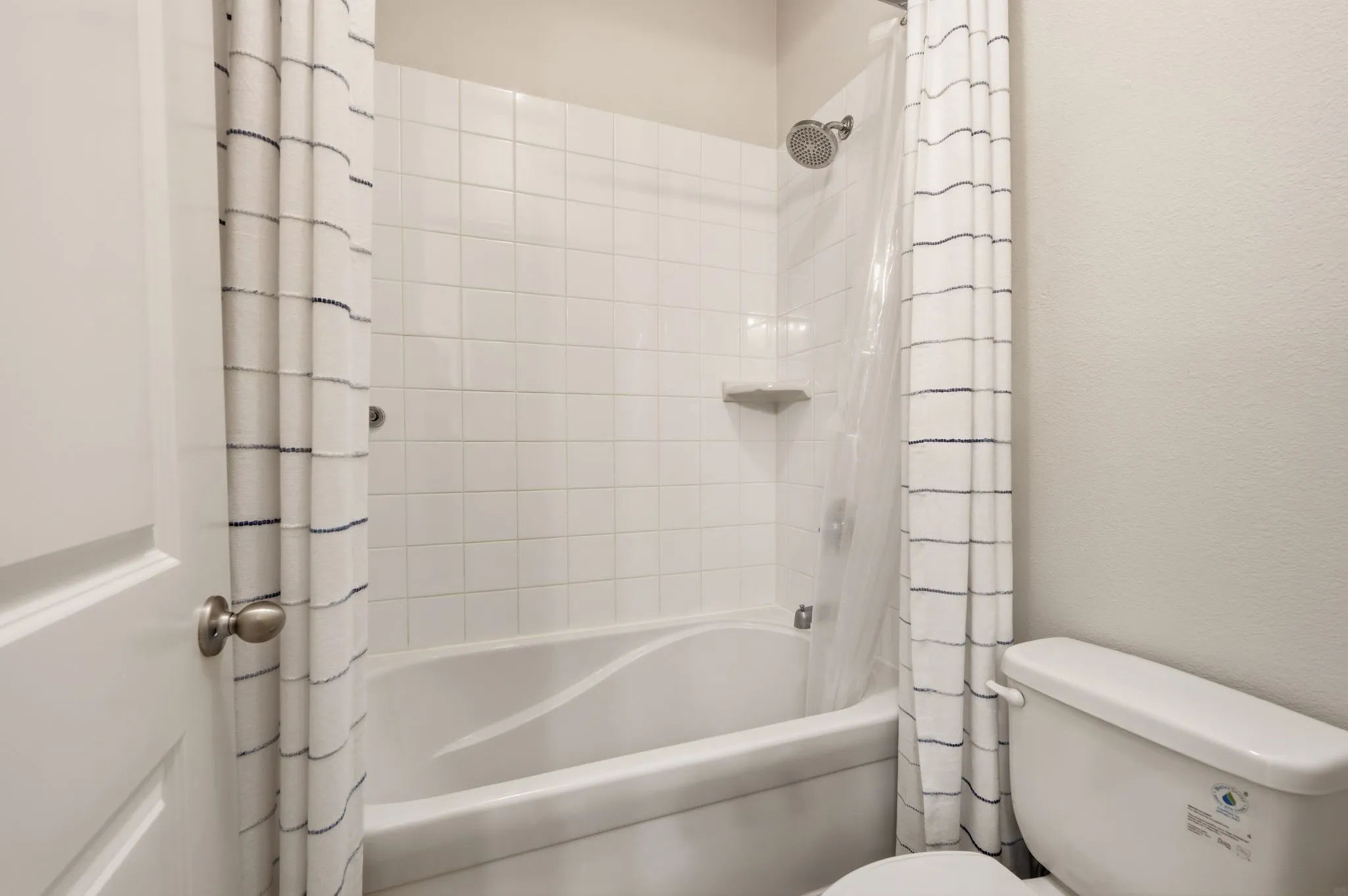 Bathroom featuring a white subway tile surround, a built-in shower niche, a chrome shower head, and a white porcelain bathtub