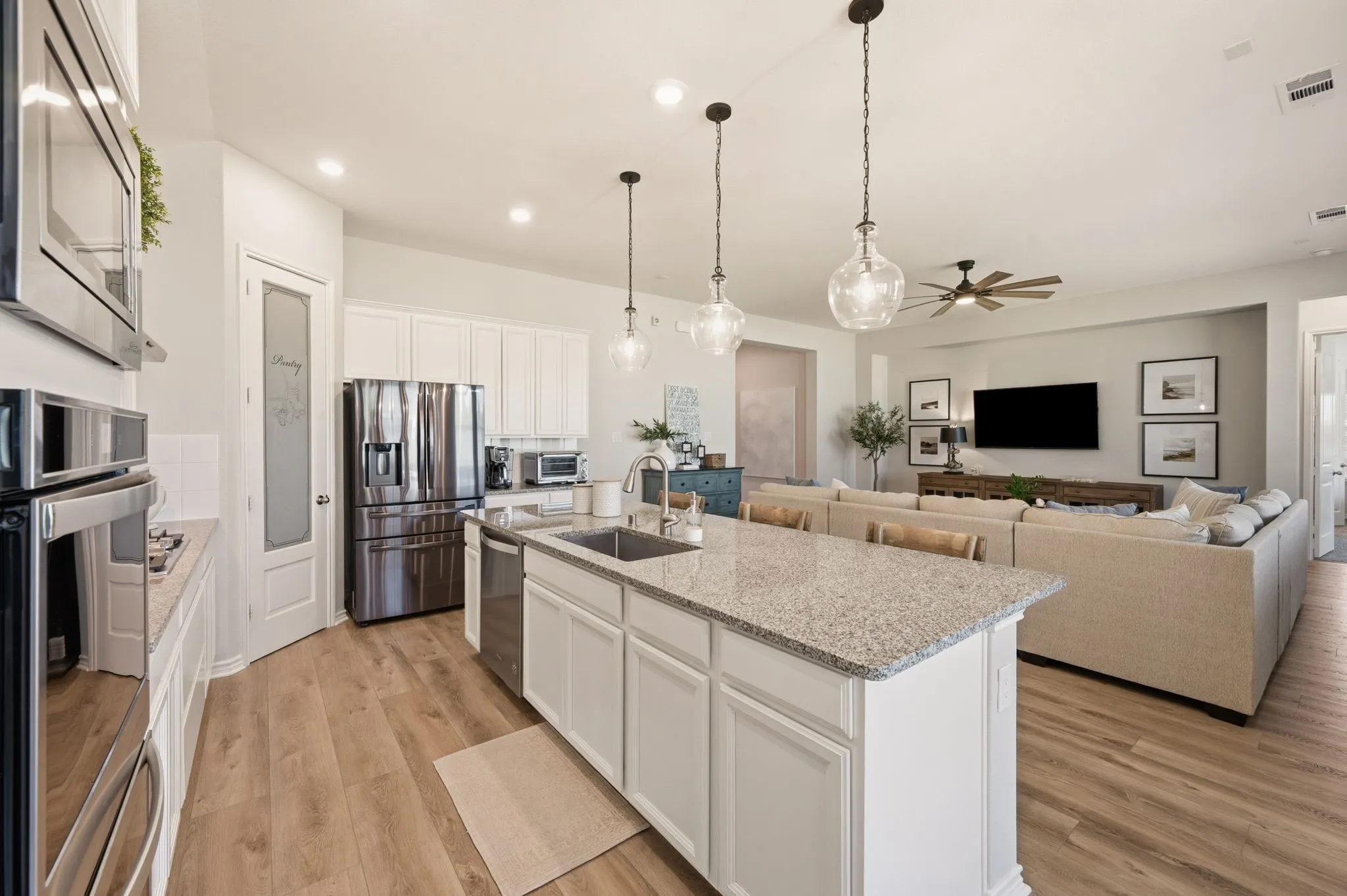 Open-concept kitchen and living area featuring wood-finish flooring, white cabinetry, stainless steel appliances, a kitchen island with stone countertops, and decorative pendant lighting