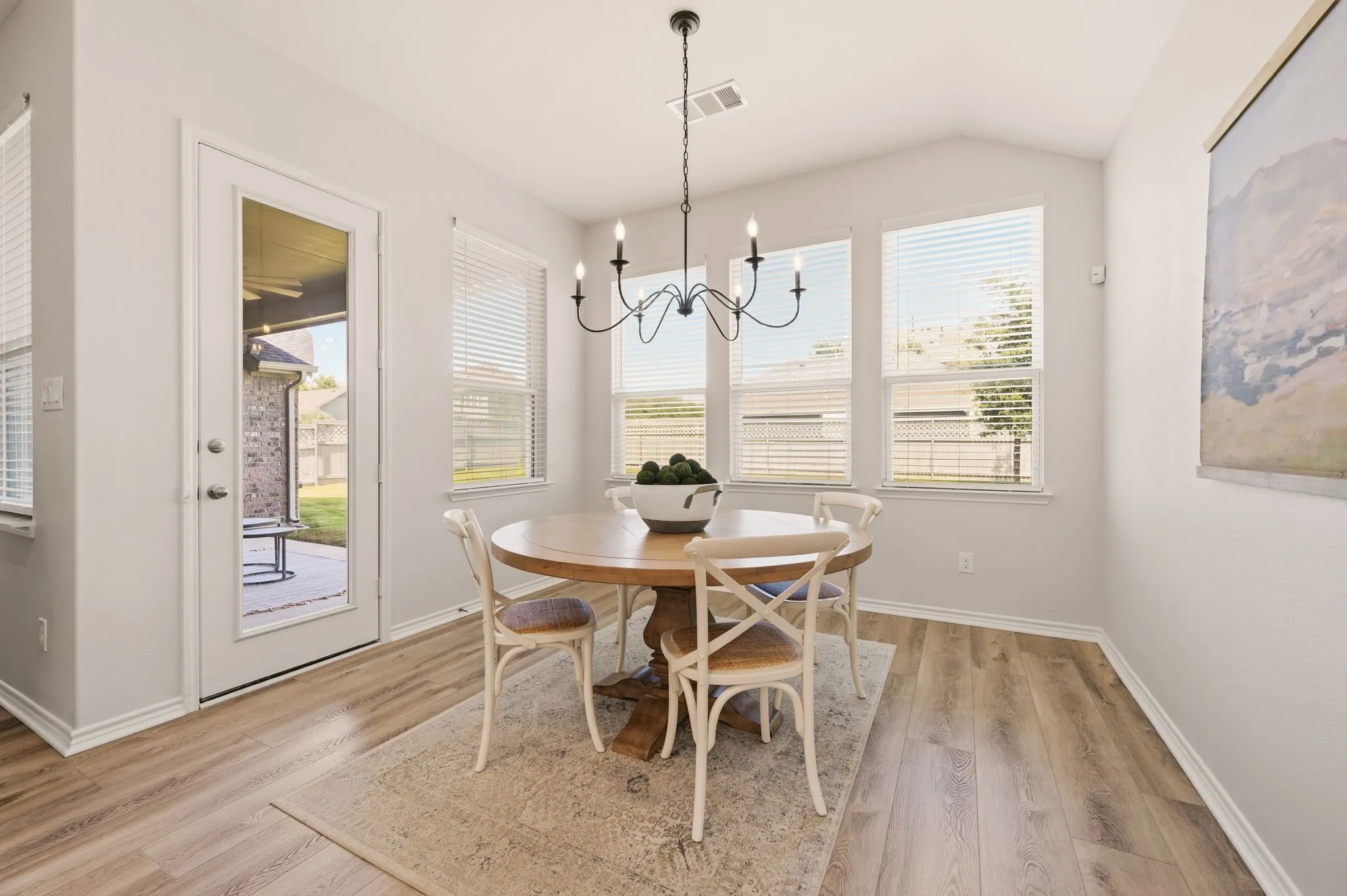 Vaulted ceiling dining area featuring wood-finish flooring, multiple windows with blinds, a black chandelier, and a full-light exterior door