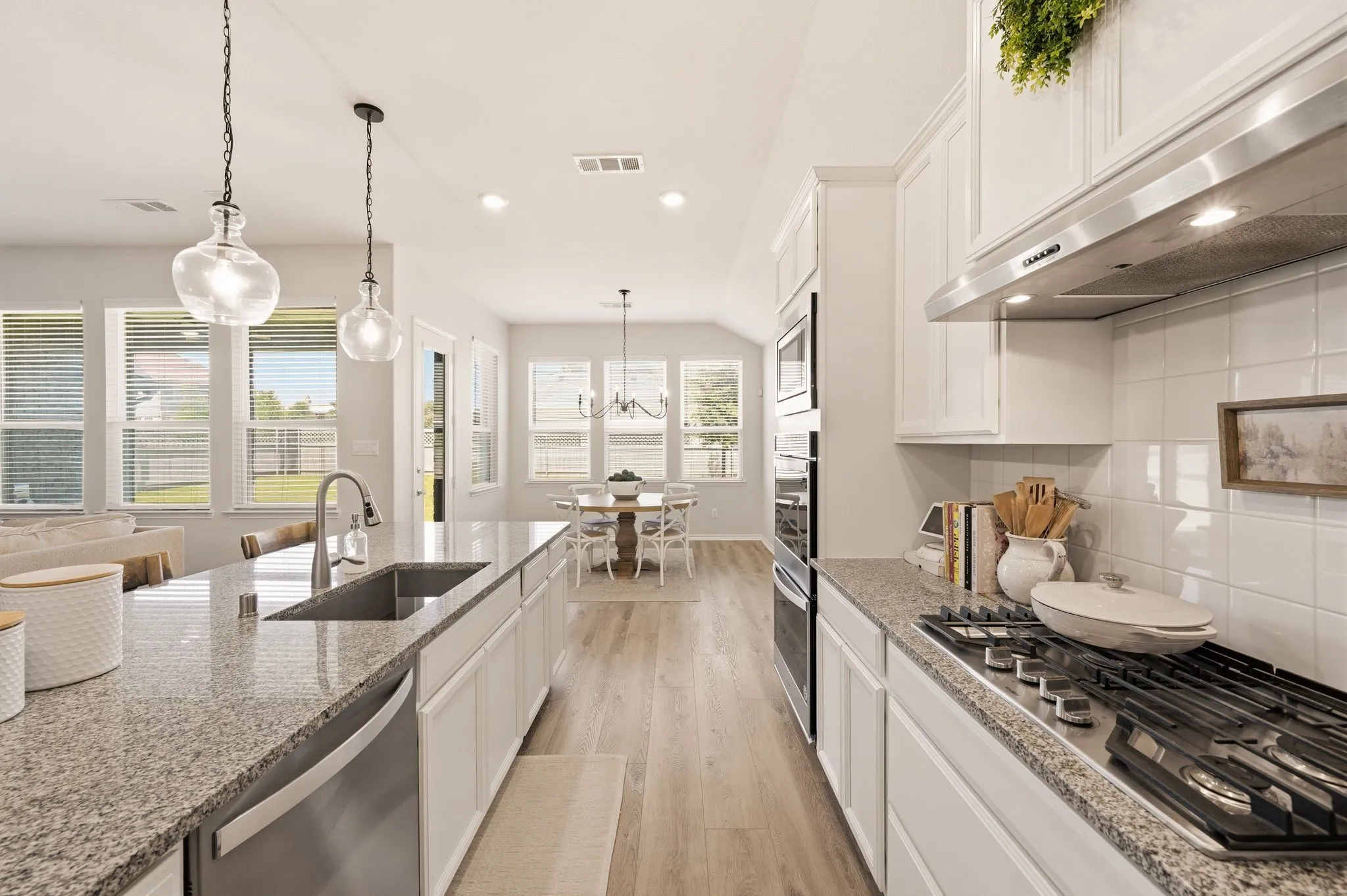 Gourmet kitchen featuring granite countertops, stainless steel appliances, white cabinetry, and wood-finish flooring