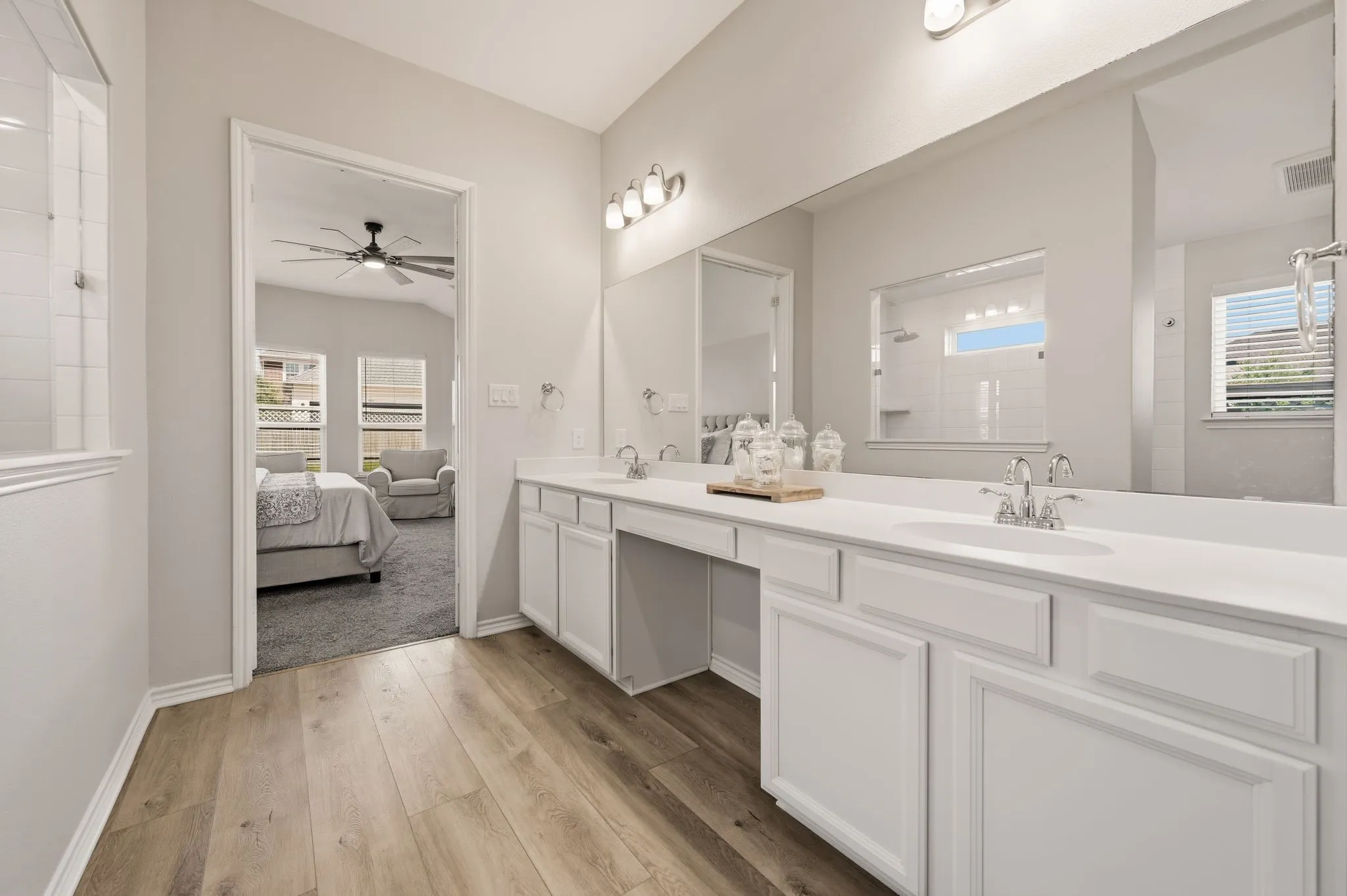 Contemporary bathroom featuring a double vanity with white cabinetry and integrated sinks, wood-finish flooring, and a large wall-mounted mirror
