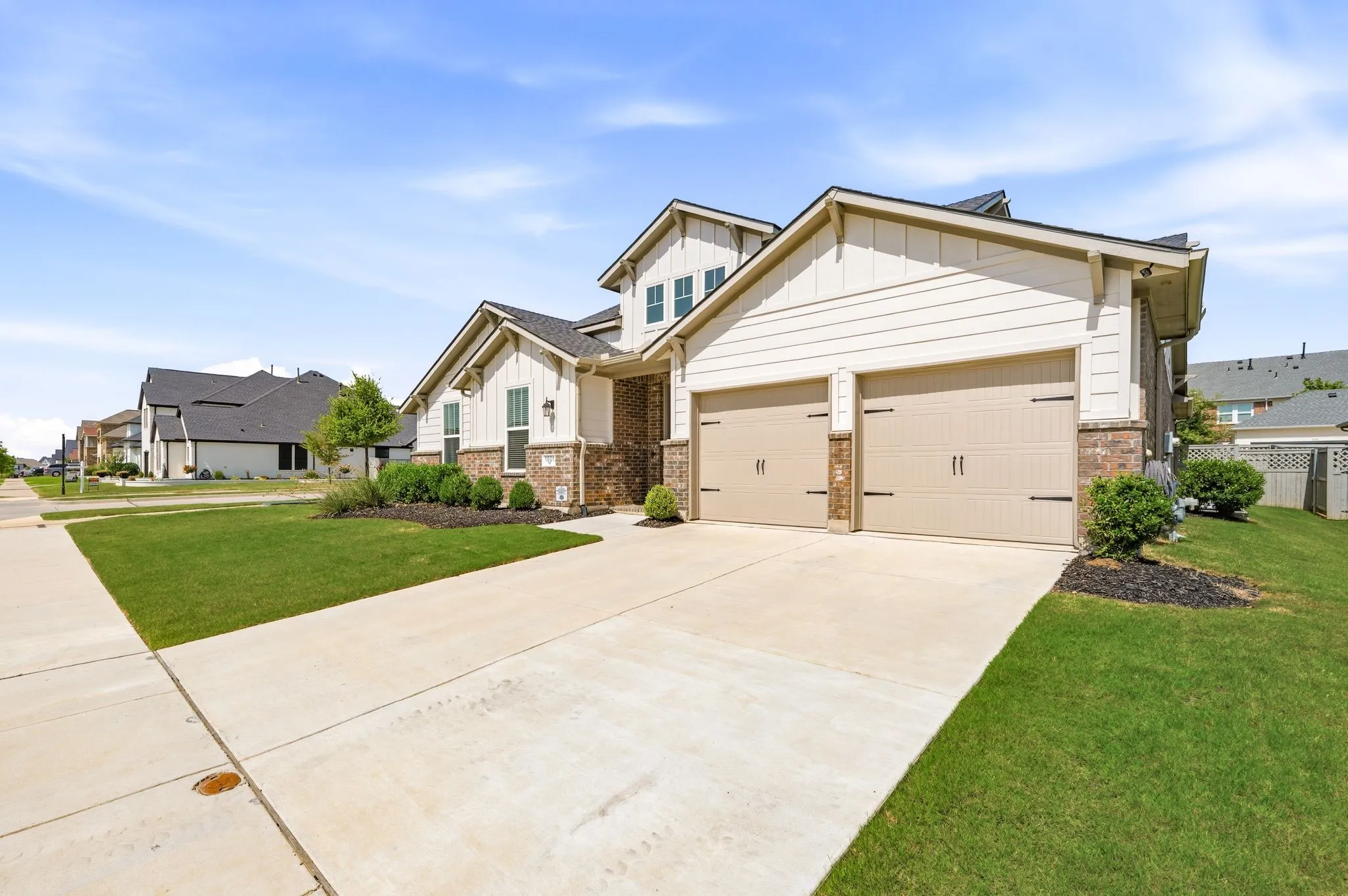 Beautiful modern facade featuring light-colored siding, brick accents, and a dual garage doors that leads into a 3 car tandem garage