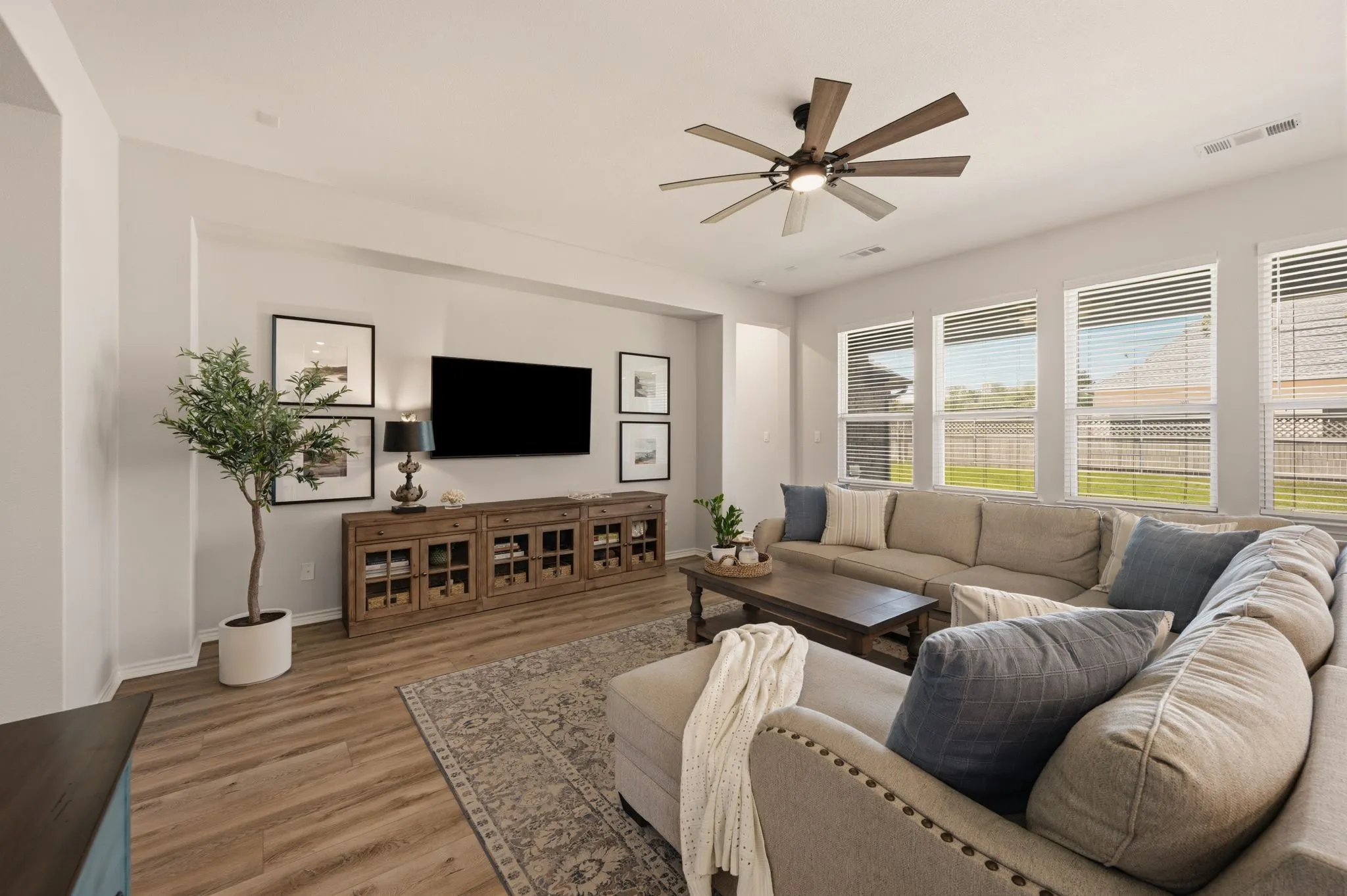 Spacious living area featuring fresh paint,  high quality LVP wood-finish flooring, updated ceiling fan, and so many windows letting in all the lovely natural light!