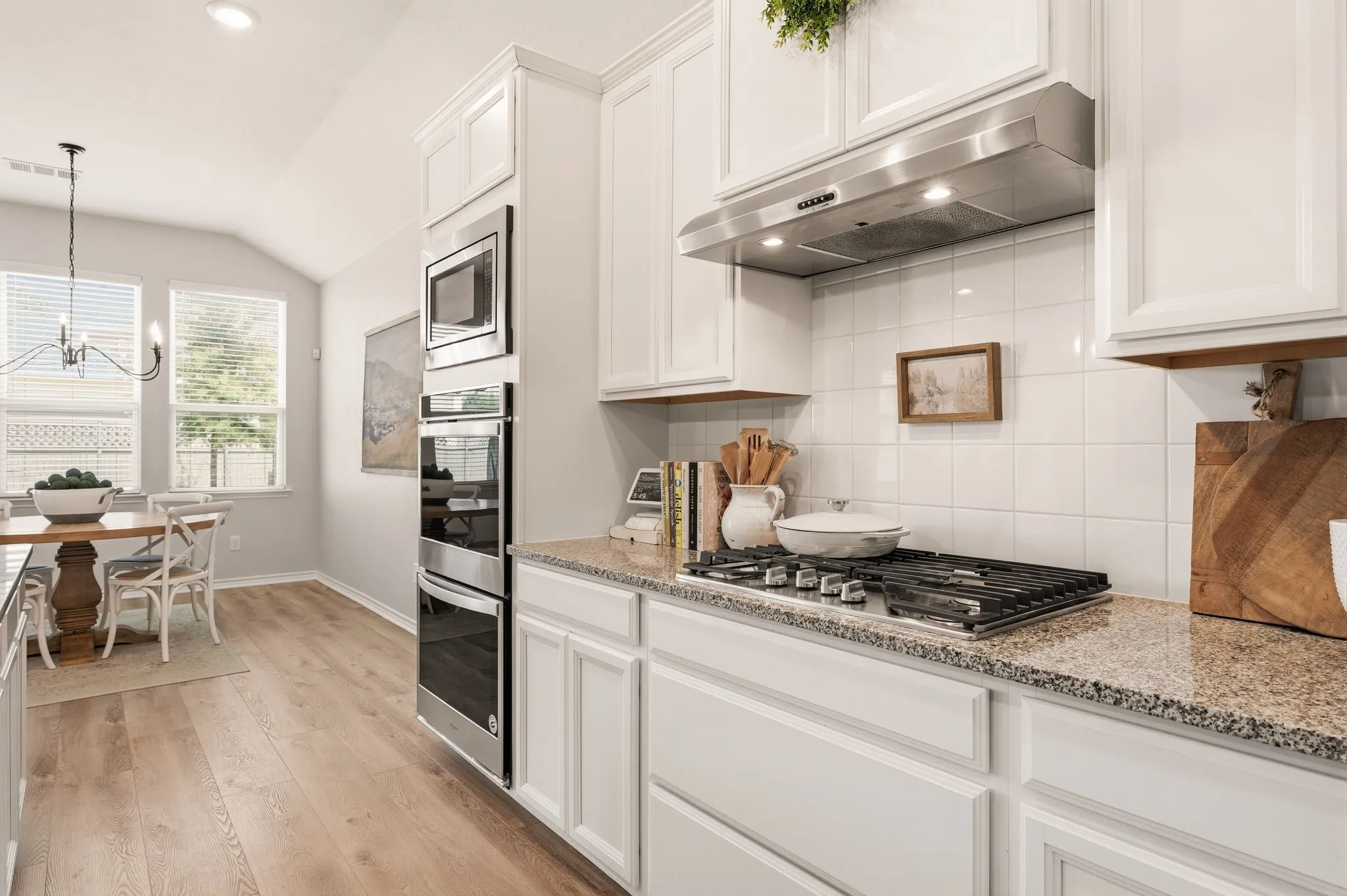 Contemporary kitchen featuring white cabinetry, granite countertops, a built-in stainless steel double oven, and a gas cooktop with a stainless steel range hood