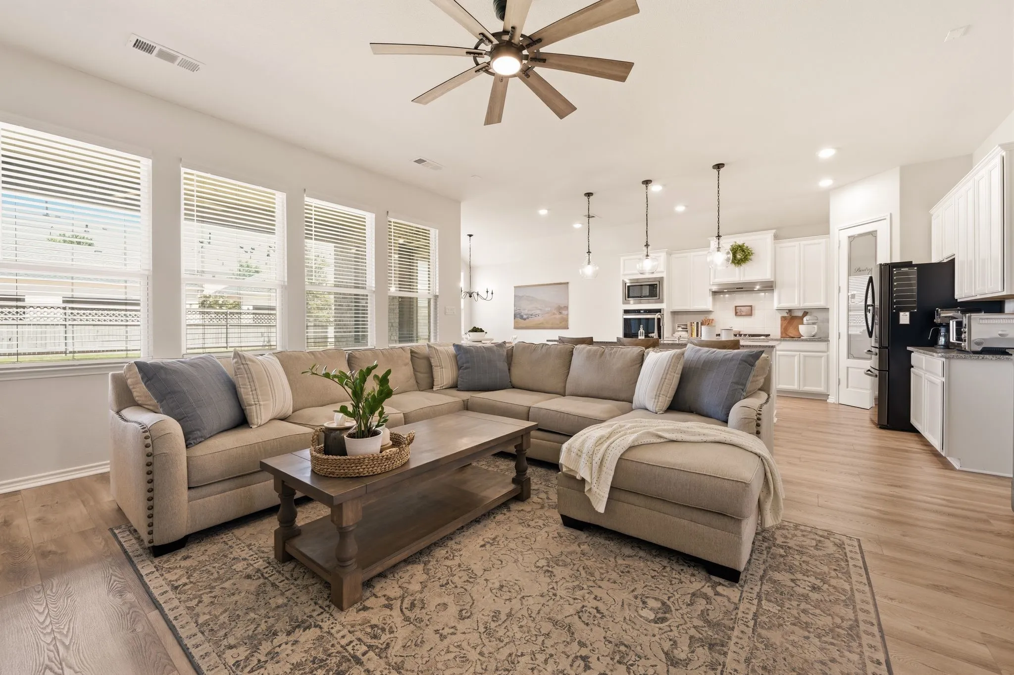 Open-concept living area with high quality LVP flooring, an updated ceiling fan, amazing windows letting in all the lovely natural light and just all the space you can enjoy your family and friends
