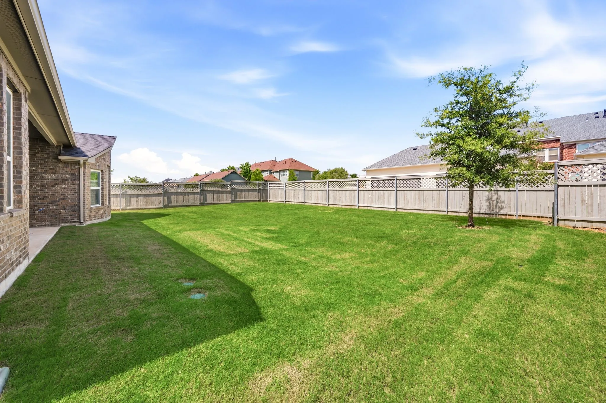 Expansive green lawn with a mature tree, featuring a wood fence with lattice accents