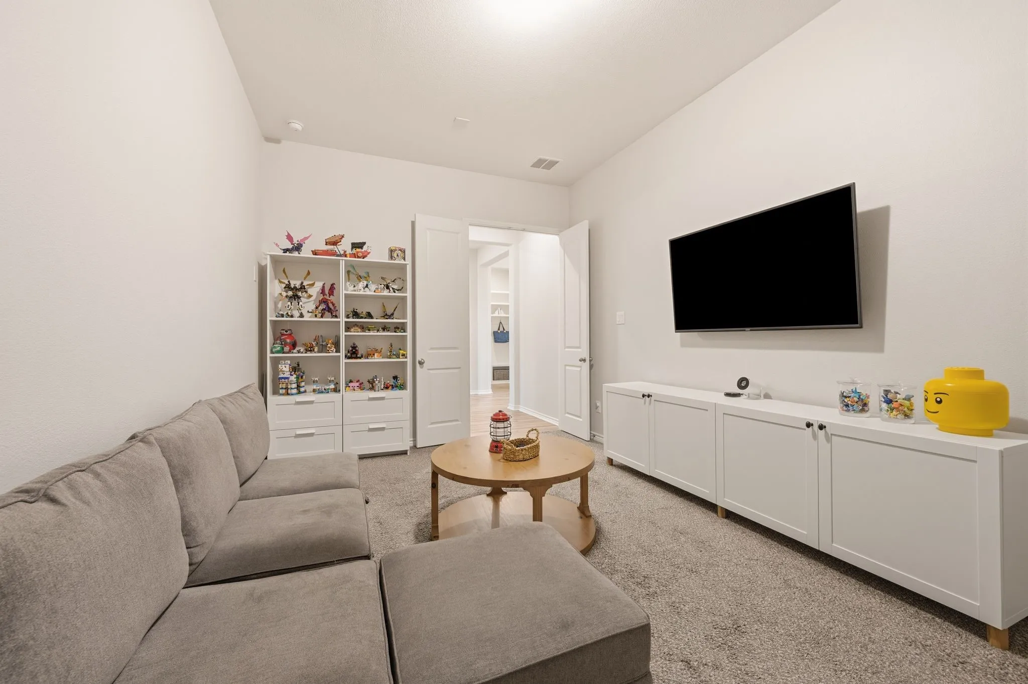 Carpeted room featuring a white built-in storage unit, a white wall-mounted media console, and an open doorway revealing a light-colored flooring