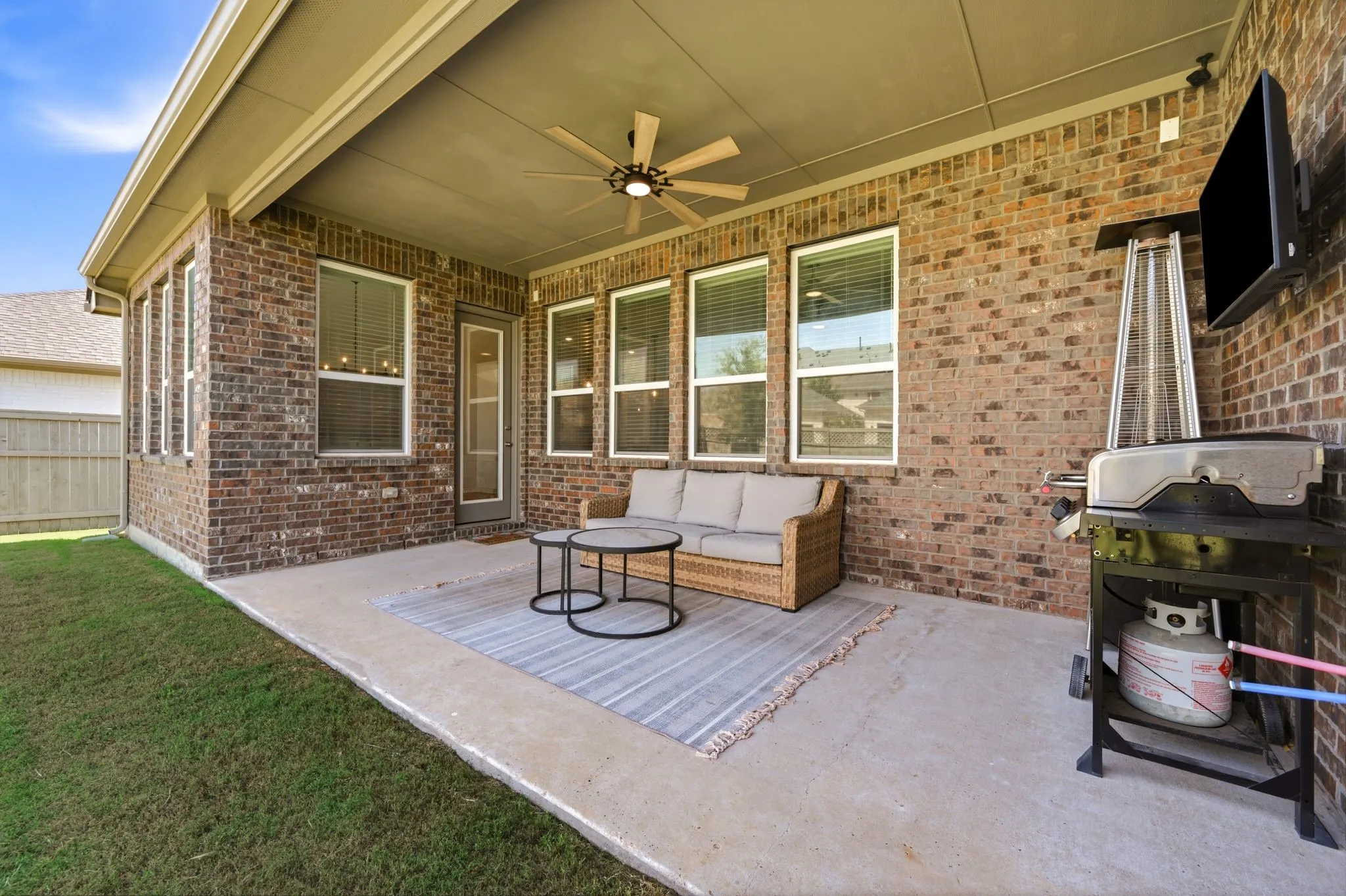 Expansive covered patio featuring brick exterior walls, multiple windows with blinds, a ceiling fan, and concrete flooring