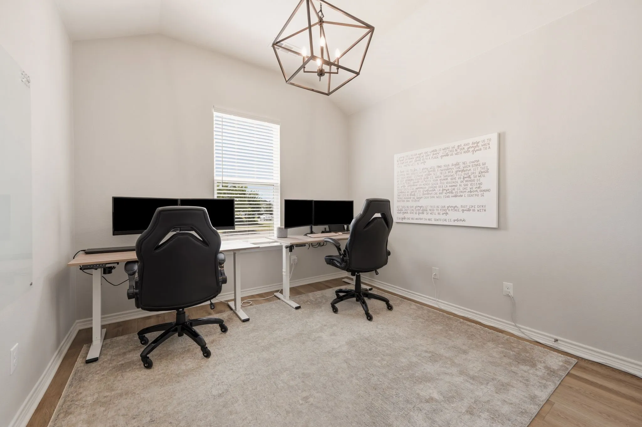 Vaulted ceiling office space featuring wood-finish flooring, a contemporary geometric light fixture, and a large window with blinds
