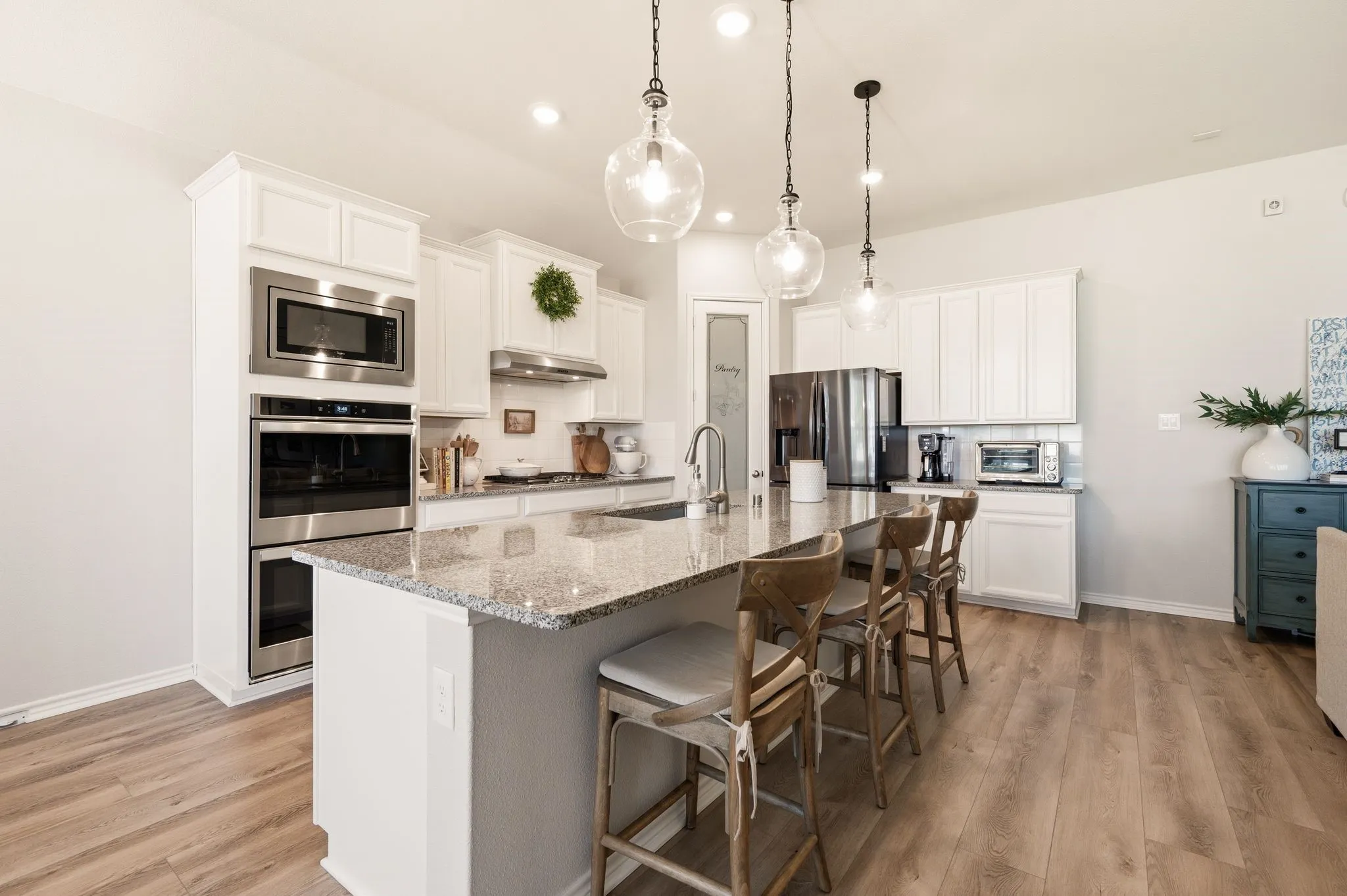 Spacious kitchen featuring an expansive center island with granite countertop, stainless steel appliances, white cabinetry, wood-finish flooring, and pendant lighting