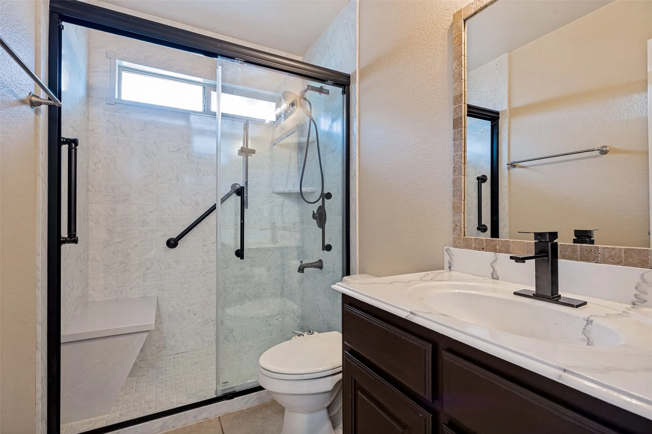 Bathroom featuring a glass-enclosed shower with a built-in bench, a transom window, and grab bars