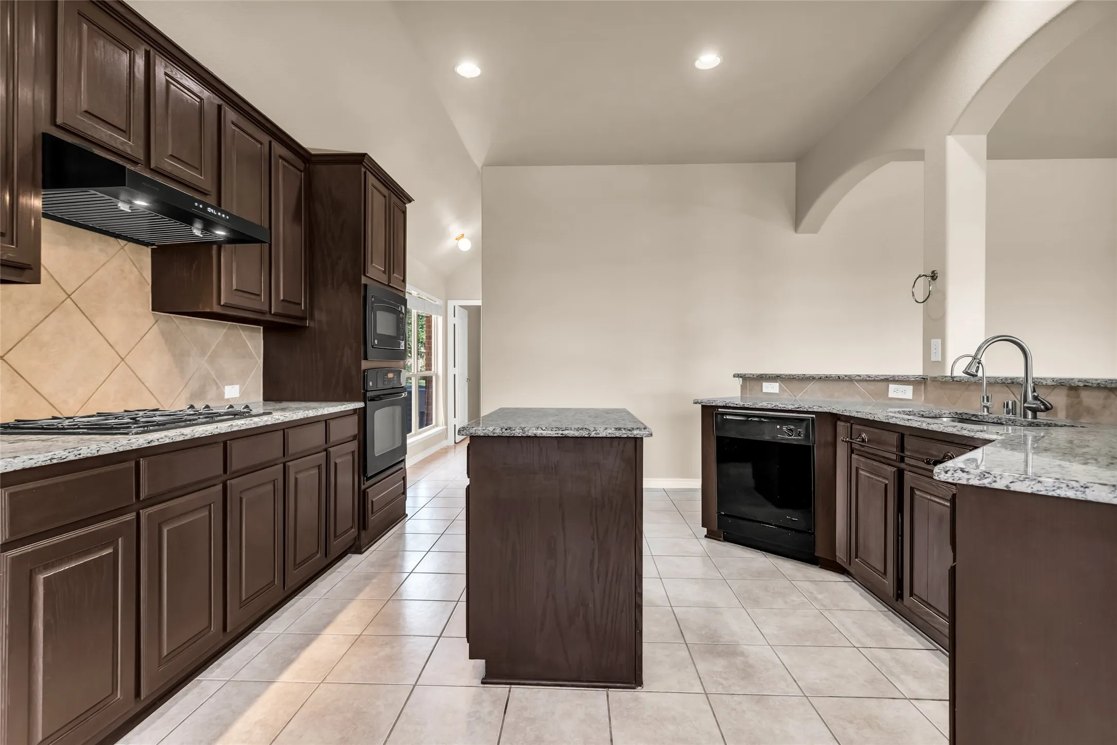 Kitchen featuring black dishwasher, arched walkways, ceiling fan, dark brown cabinets, and open floor plan