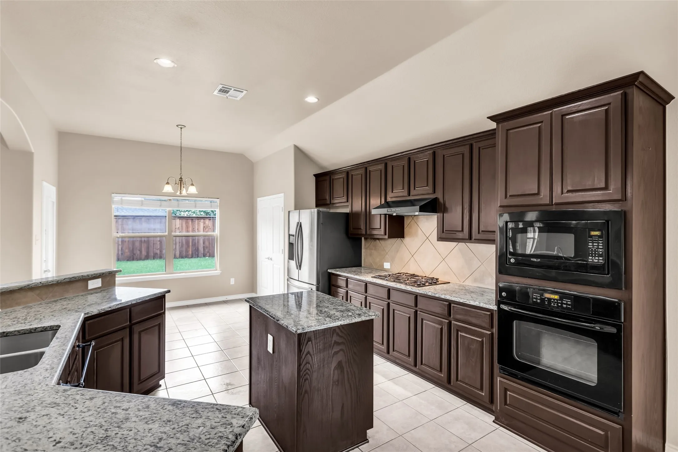 Kitchen featuring black appliances, under cabinet range hood, dark brown cabinetry, a center island, and backsplash