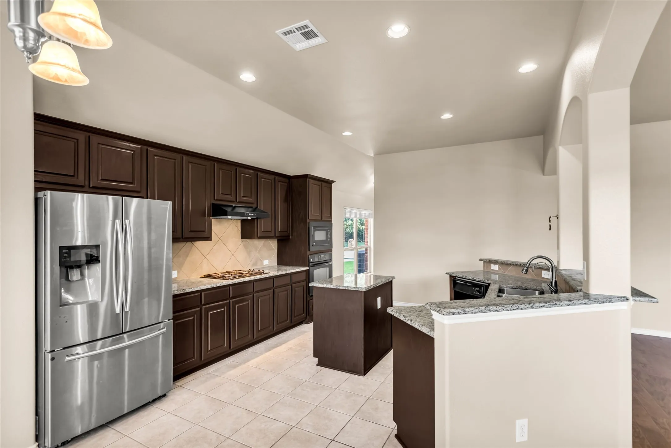 Kitchen with black appliances, under cabinet range hood, a center island, backsplash, and light tile patterned flooring
