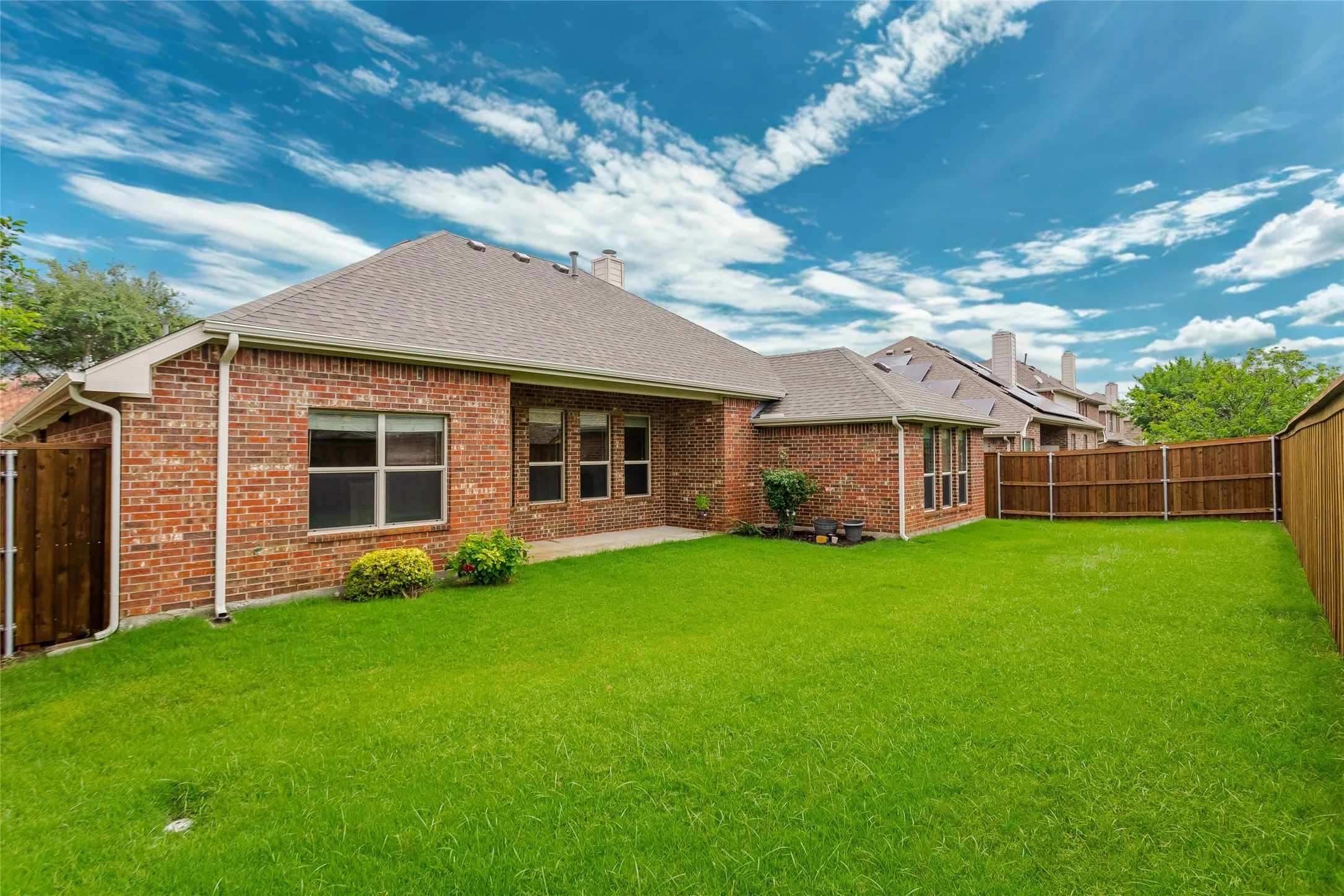 Rear view of property with fairly new fenced backyard, roof with shingles, brick siding, and a chimney.
