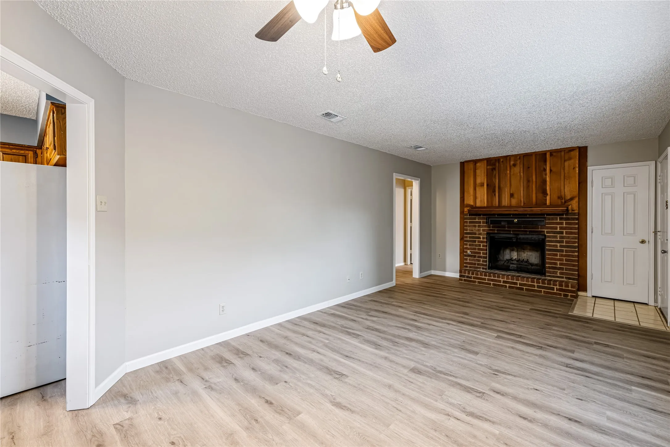 Unfurnished living room with baseboards, light wood finished floors, ceiling fan, and a textured ceiling