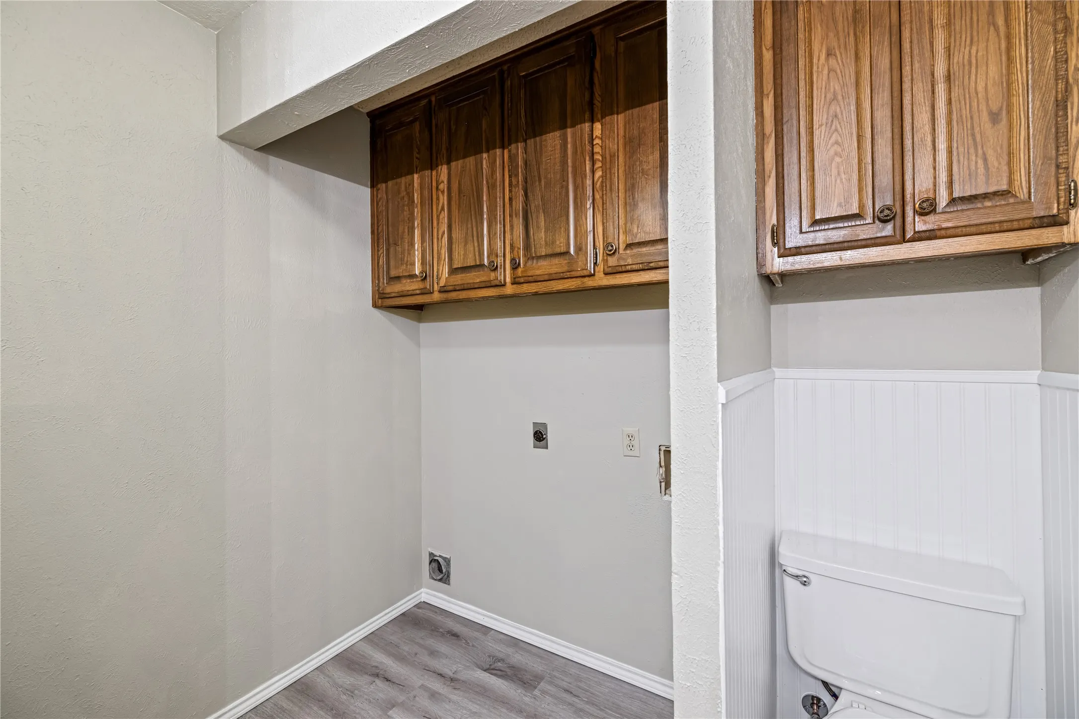 Washroom with baseboards, light wood-style floors, wainscoting, and electric dryer hookup