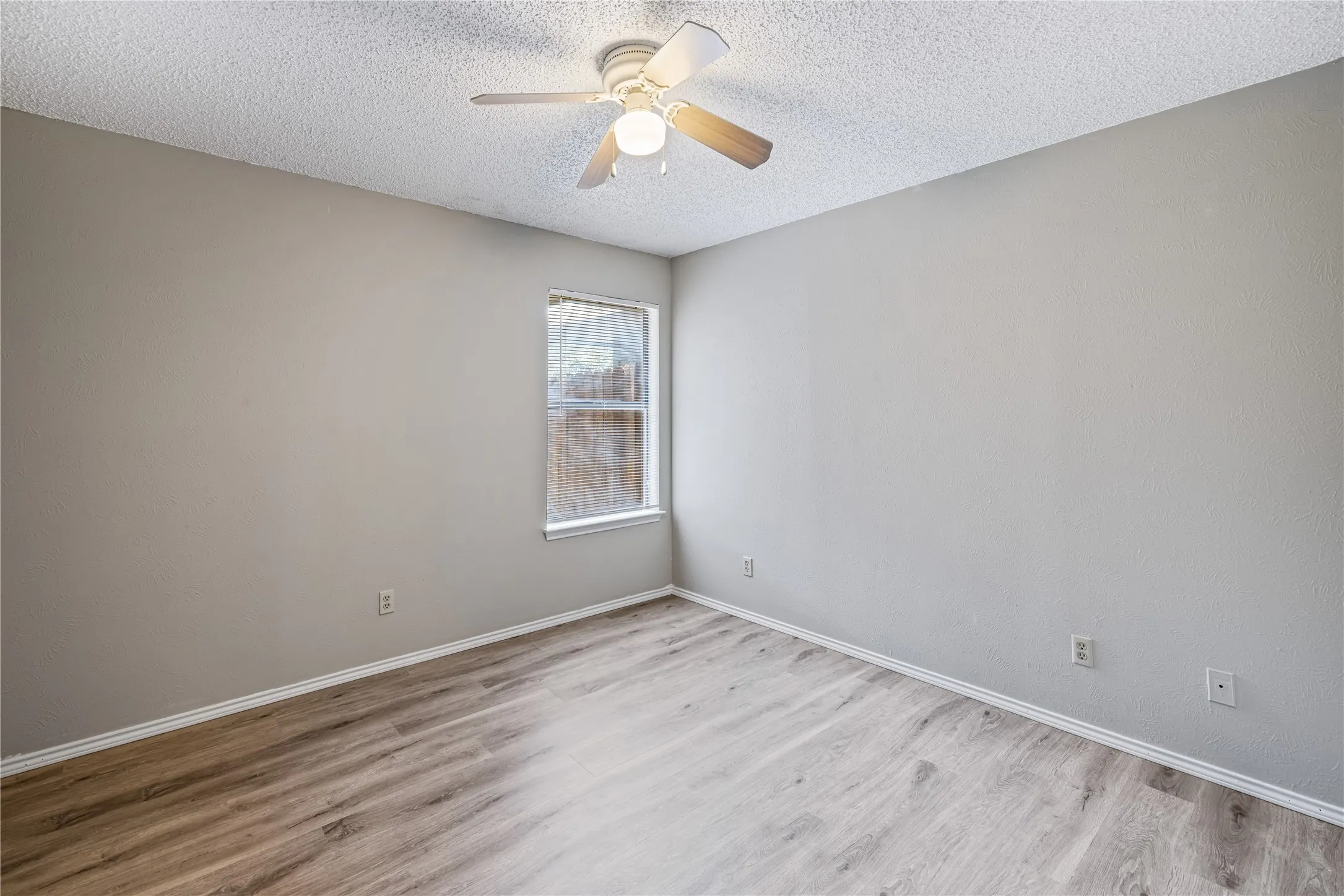 Spare room with a textured ceiling, wood finished floors, baseboards, and ceiling fan